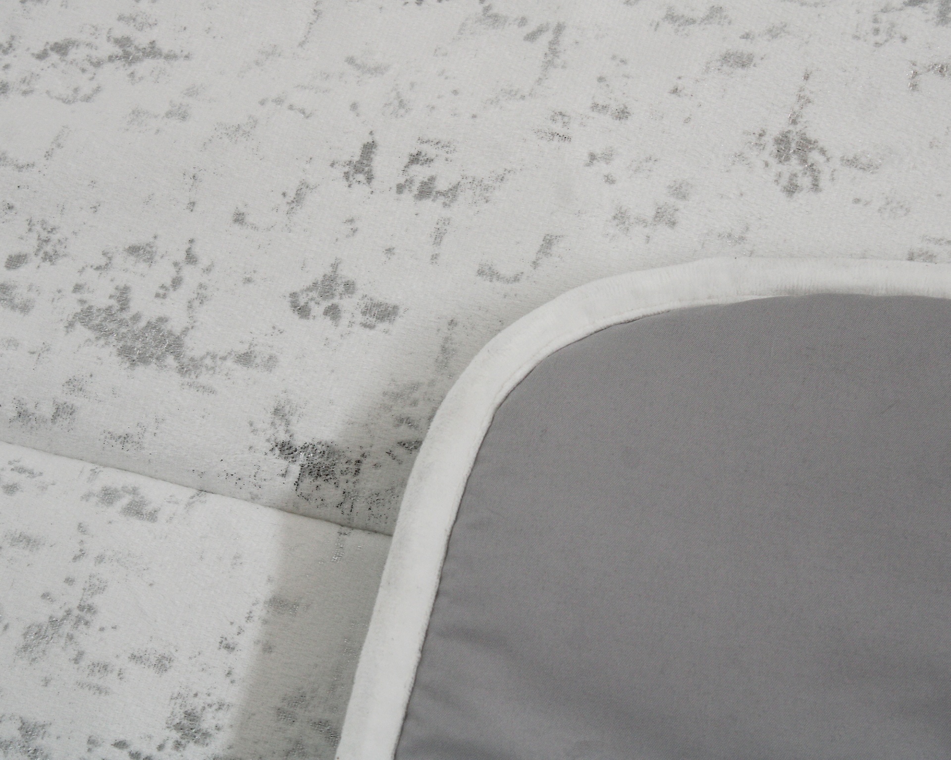 tecido cinzento com borda branca sobre superfície branca com manchas cinzentas