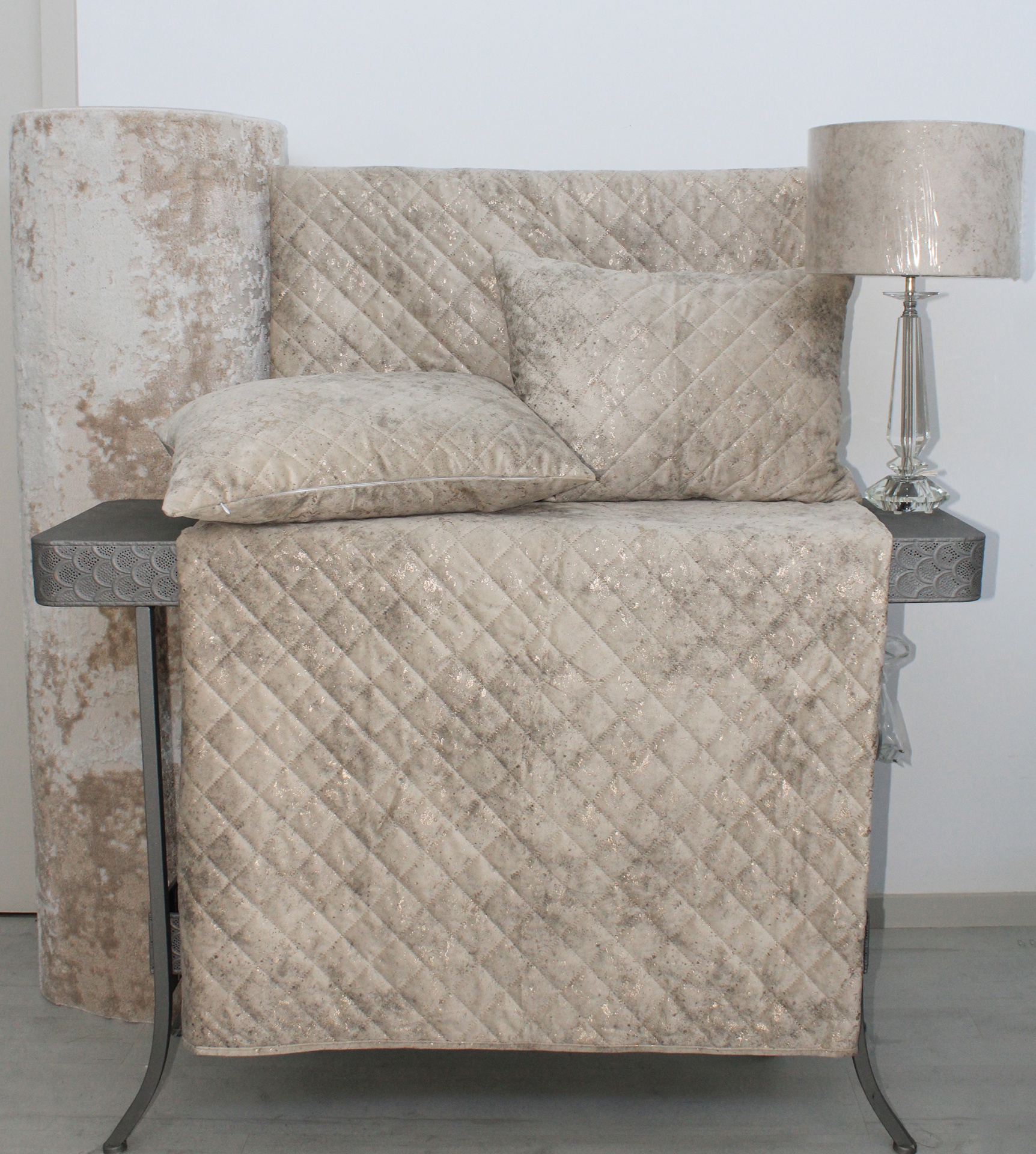 Conjunto têxtil bege de veludo com padrão de losangos numa mesa metálica com candeeiro