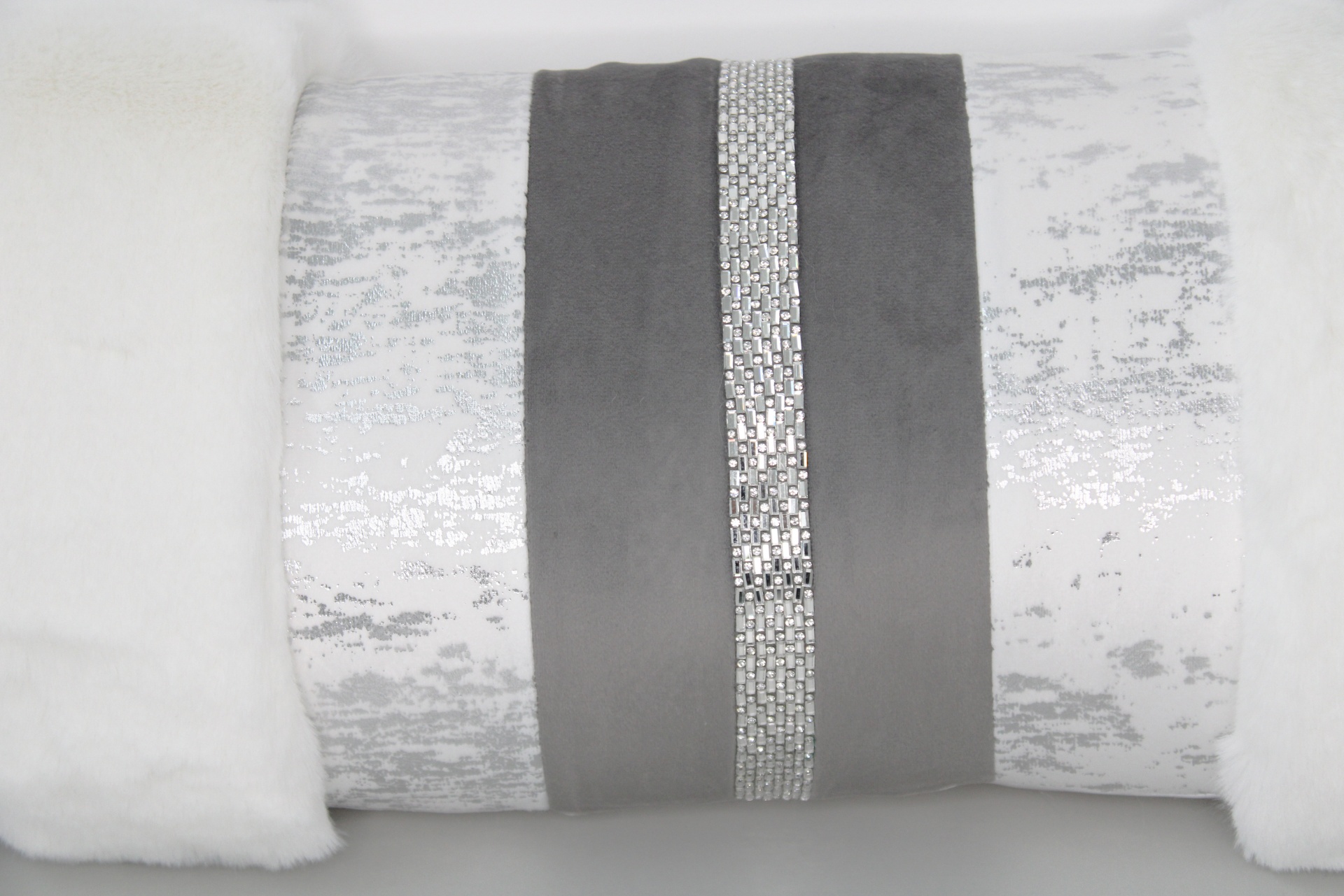 Almofada decorativa cinza e branca com faixa brilhante central e bordas felpudas