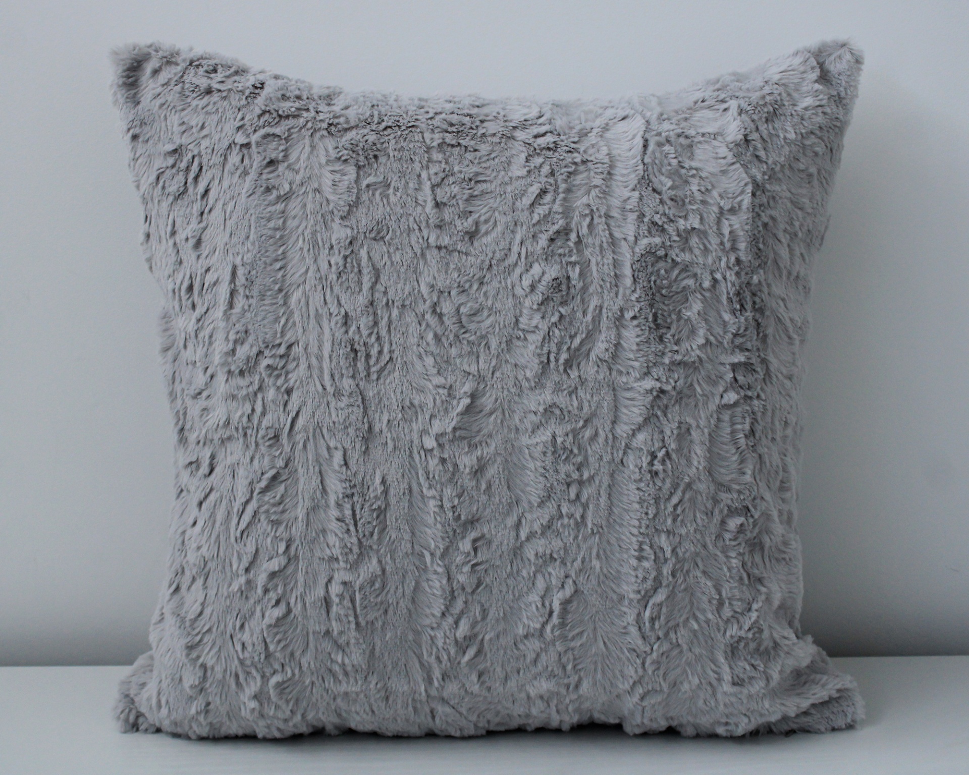 Almofada felpuda cinzenta clara numa superfície branca