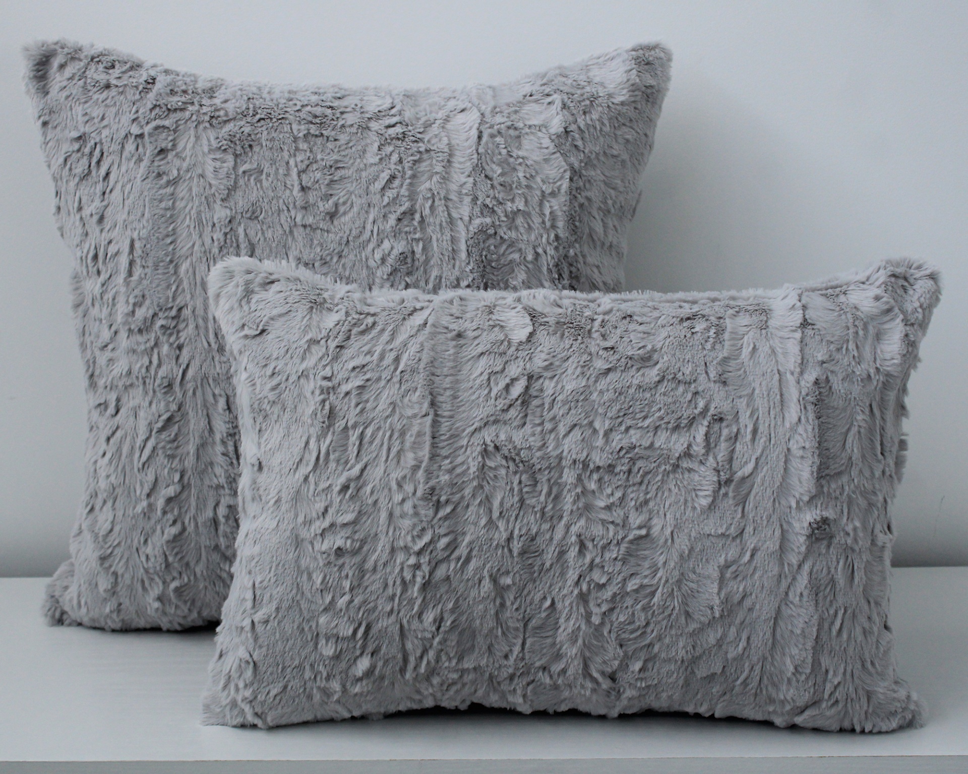 Duas almofadas felpudas cinzentas sobre superfície branca