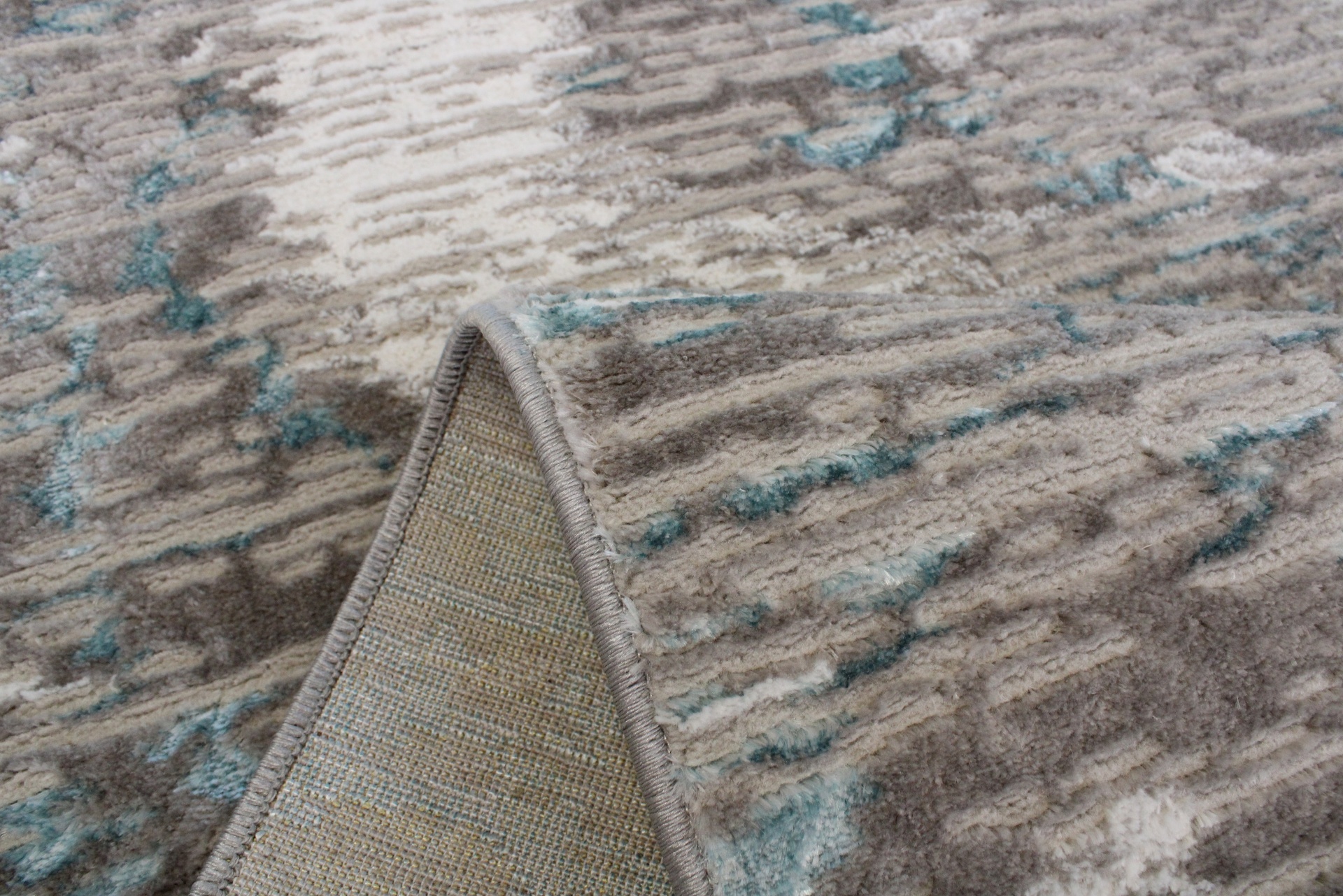 Tapete com padrão abstrato em tons bége, castanho e azul, parcialmente dobrado para mostrar o verso.