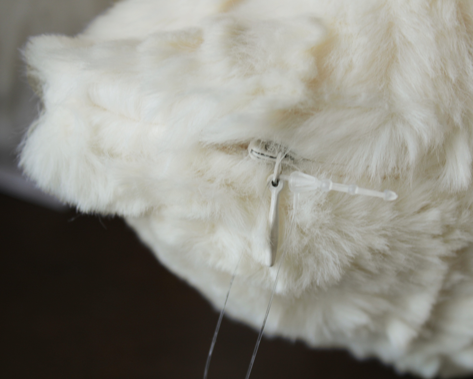 Produto felpudo branco com gancho de plástico transparente em fundo escuro