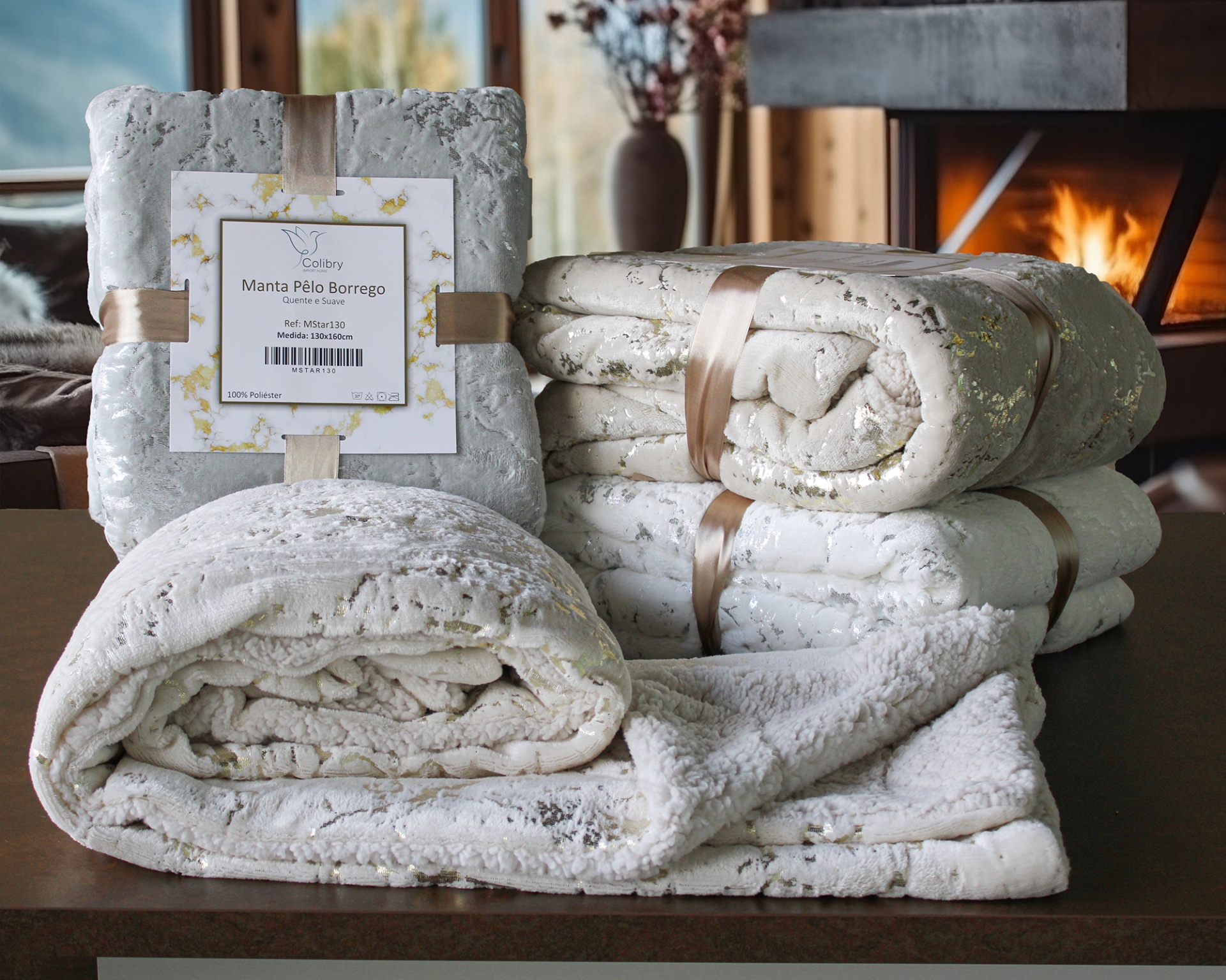 Mantas Pêlo Borrego cinza claro com detalhes dourados e rótulo em ambiente com lareira