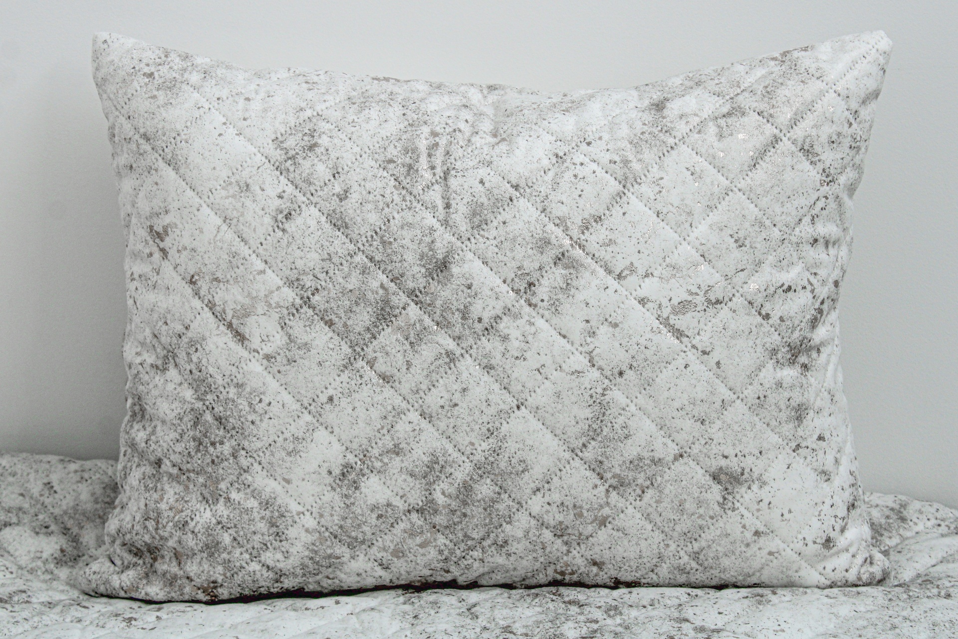 Travesseiro retangular cinzento claro com padrão matelassê colocado sobre tecido semelhante