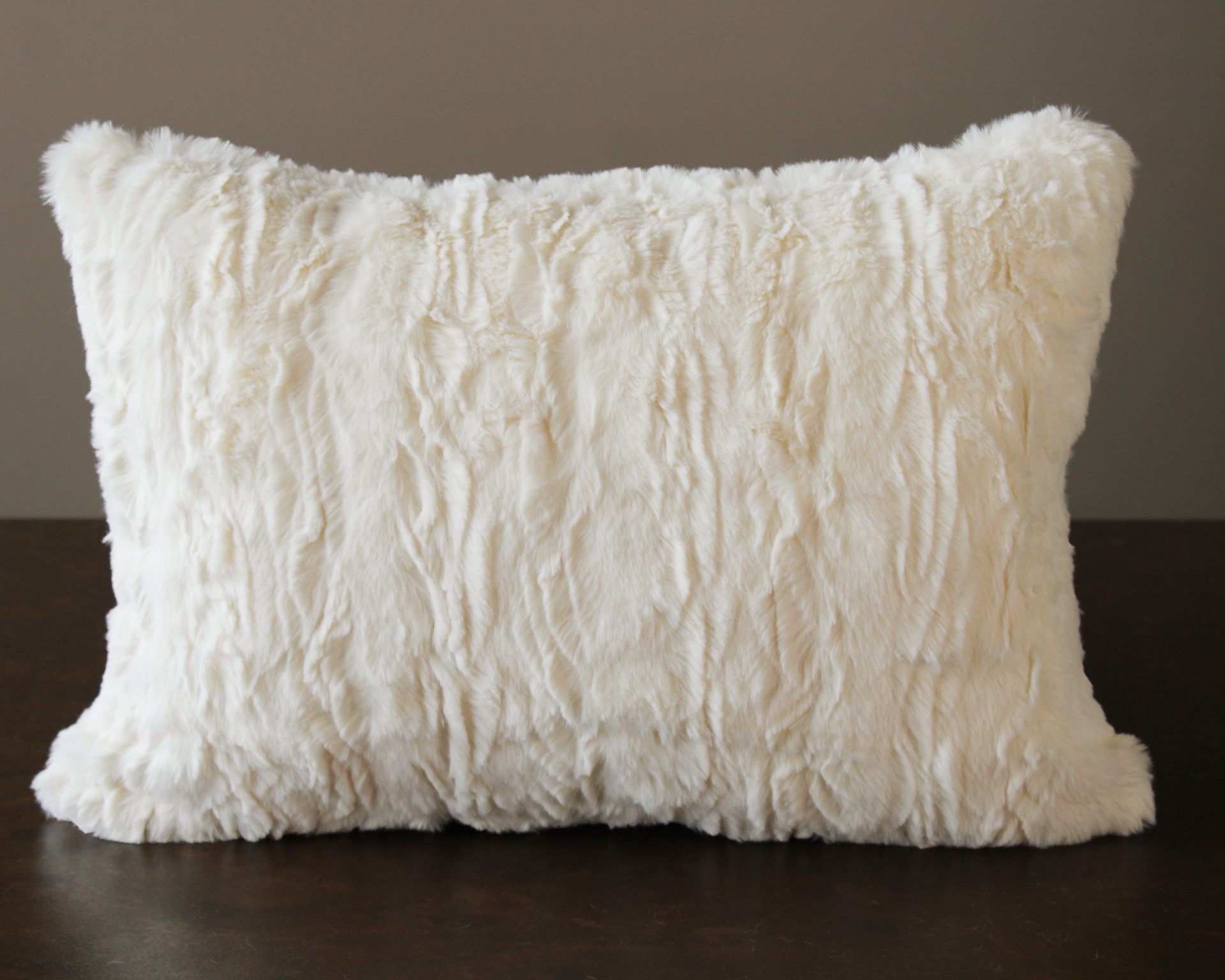 Almofada rectangular creme felpuda sobre superfície escura com fundo cinza