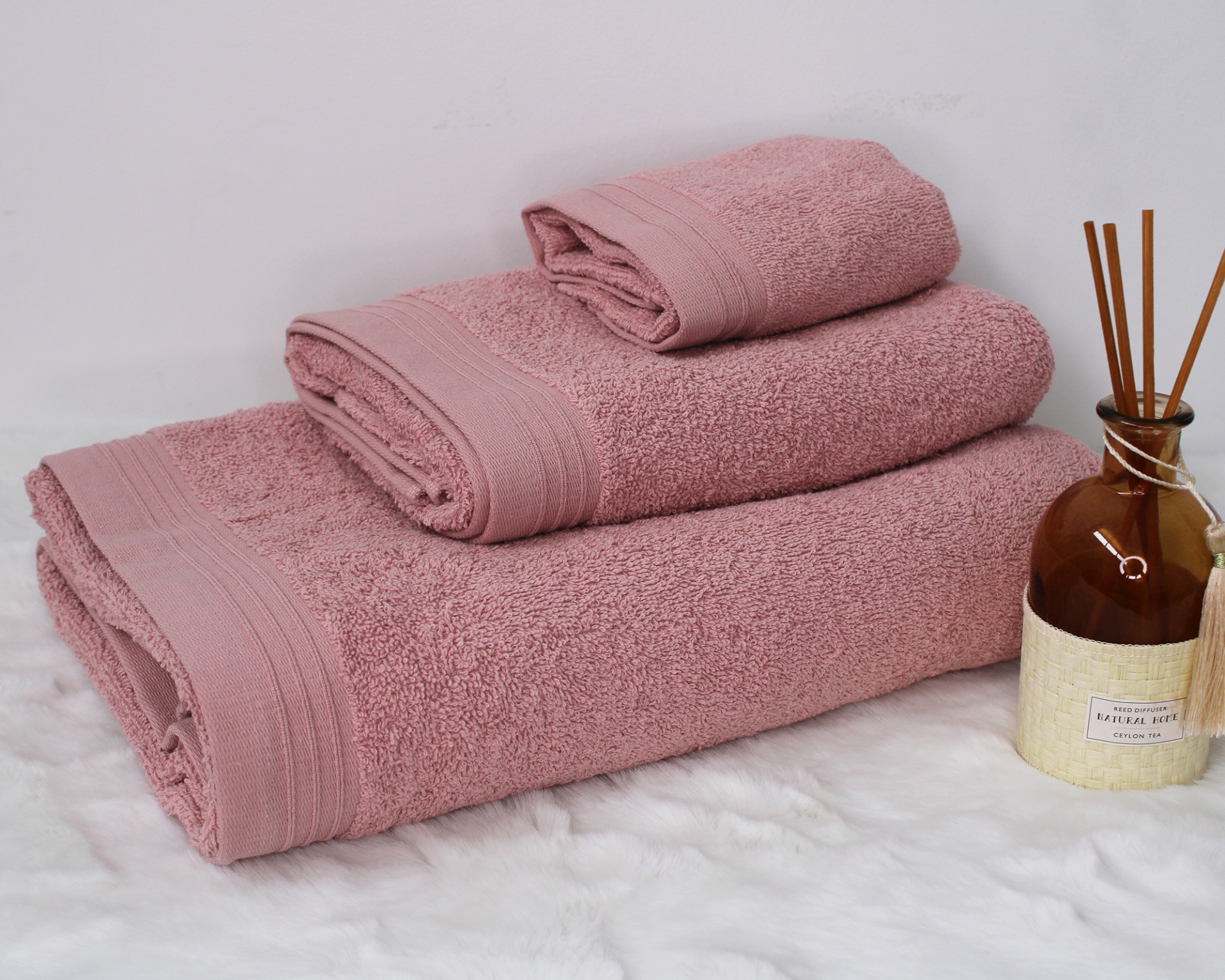 Conjunto de toalhas rosa empilhadas ao lado de difusor de ambiente