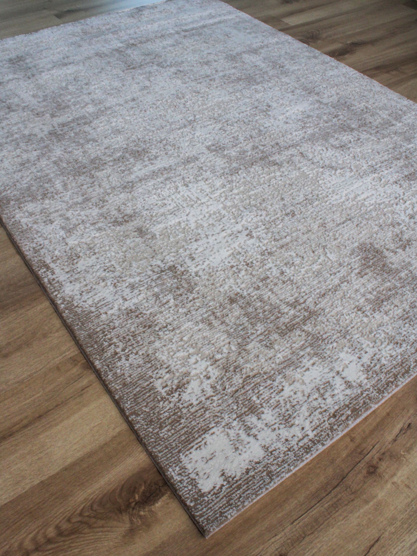 Tapete rectangular bege e castanho claro com padrão abstrato sobre chão de madeira