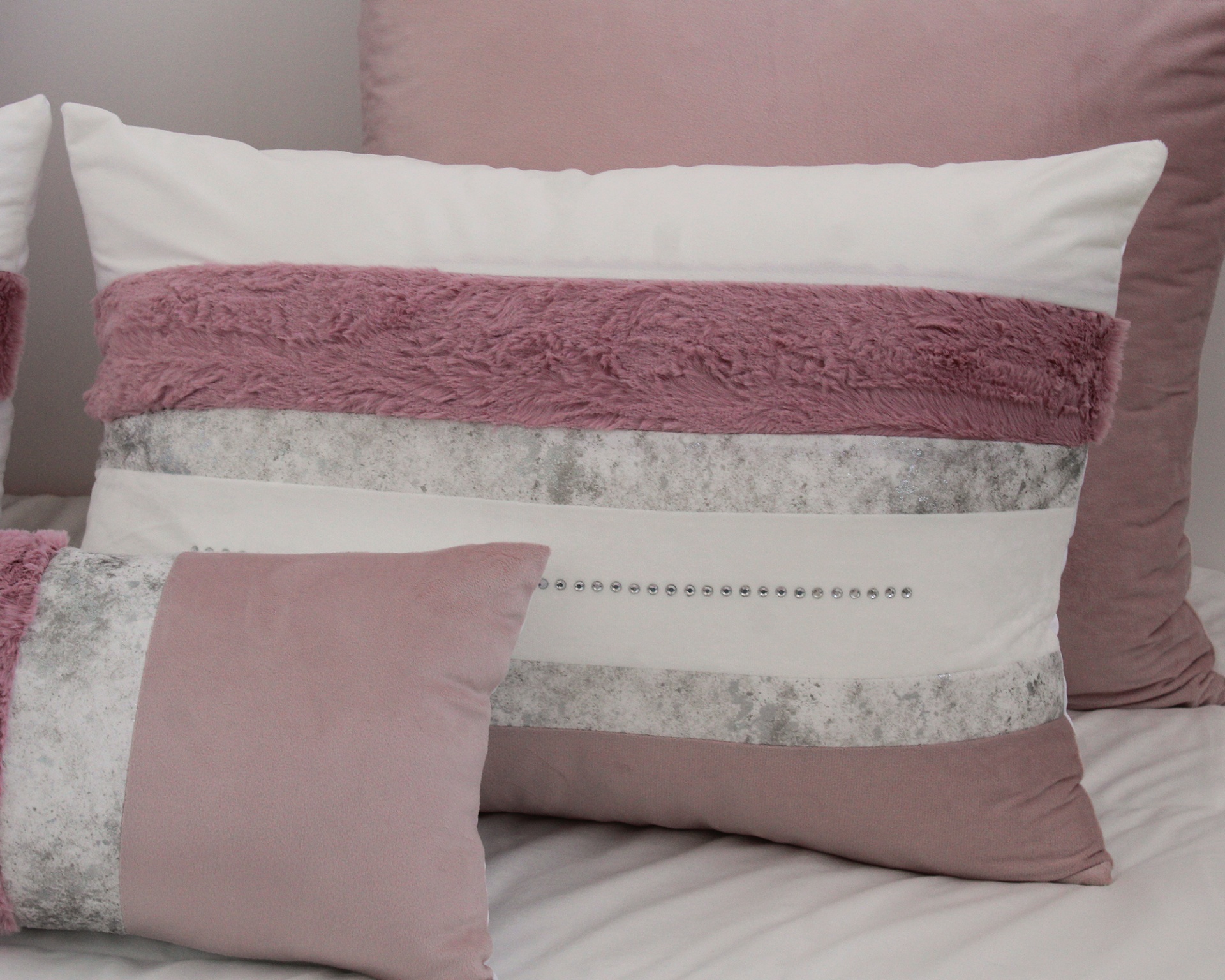 Almofadas decorativas em tons de rosa, branco e cinza com texturas e tachas