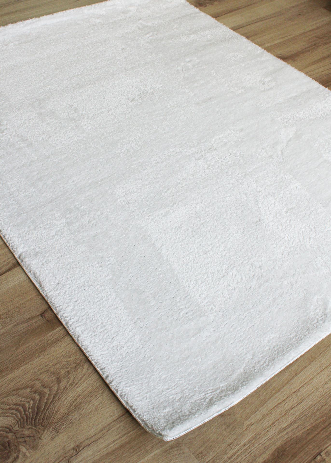 Tapete felpudo branco sobre chão de madeira clara