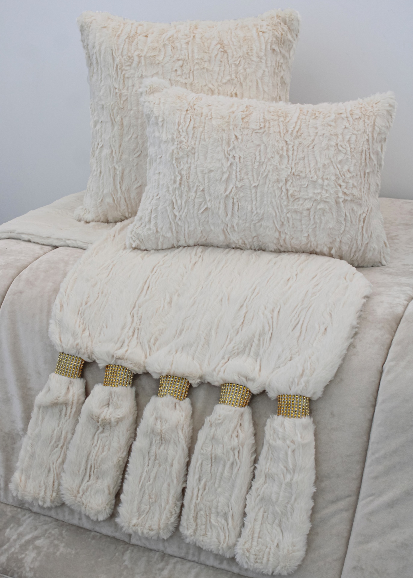 Conjunto de almofadas e manta creme com franjas e strass dourado sobre cama clara