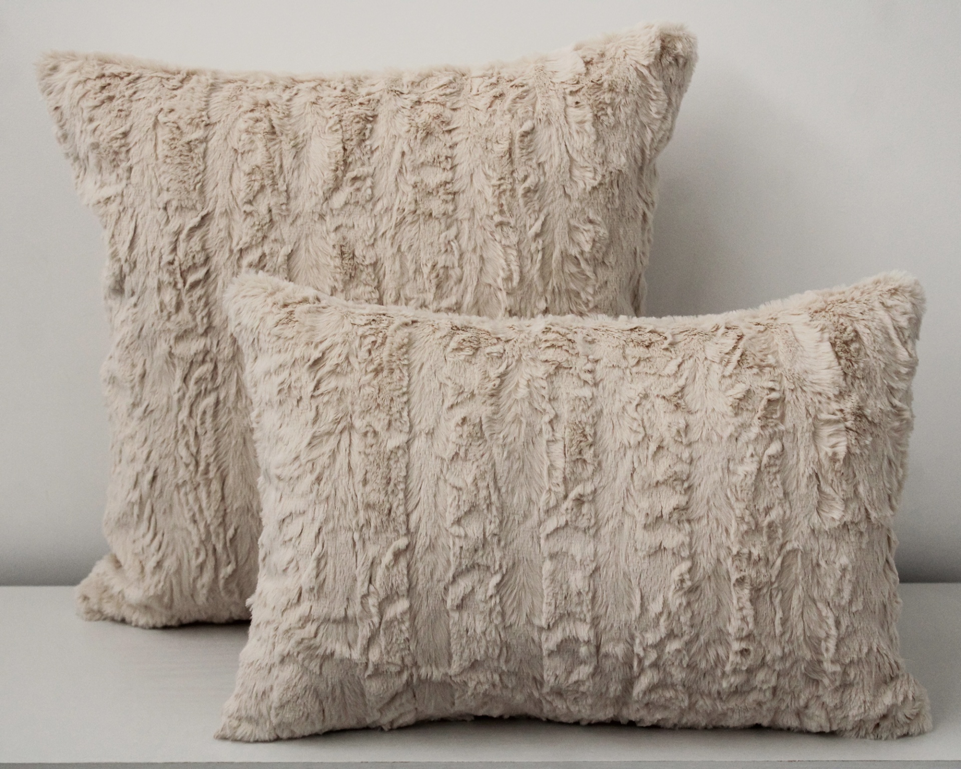 Duas almofadas peludas bege claro sobre superfície branca