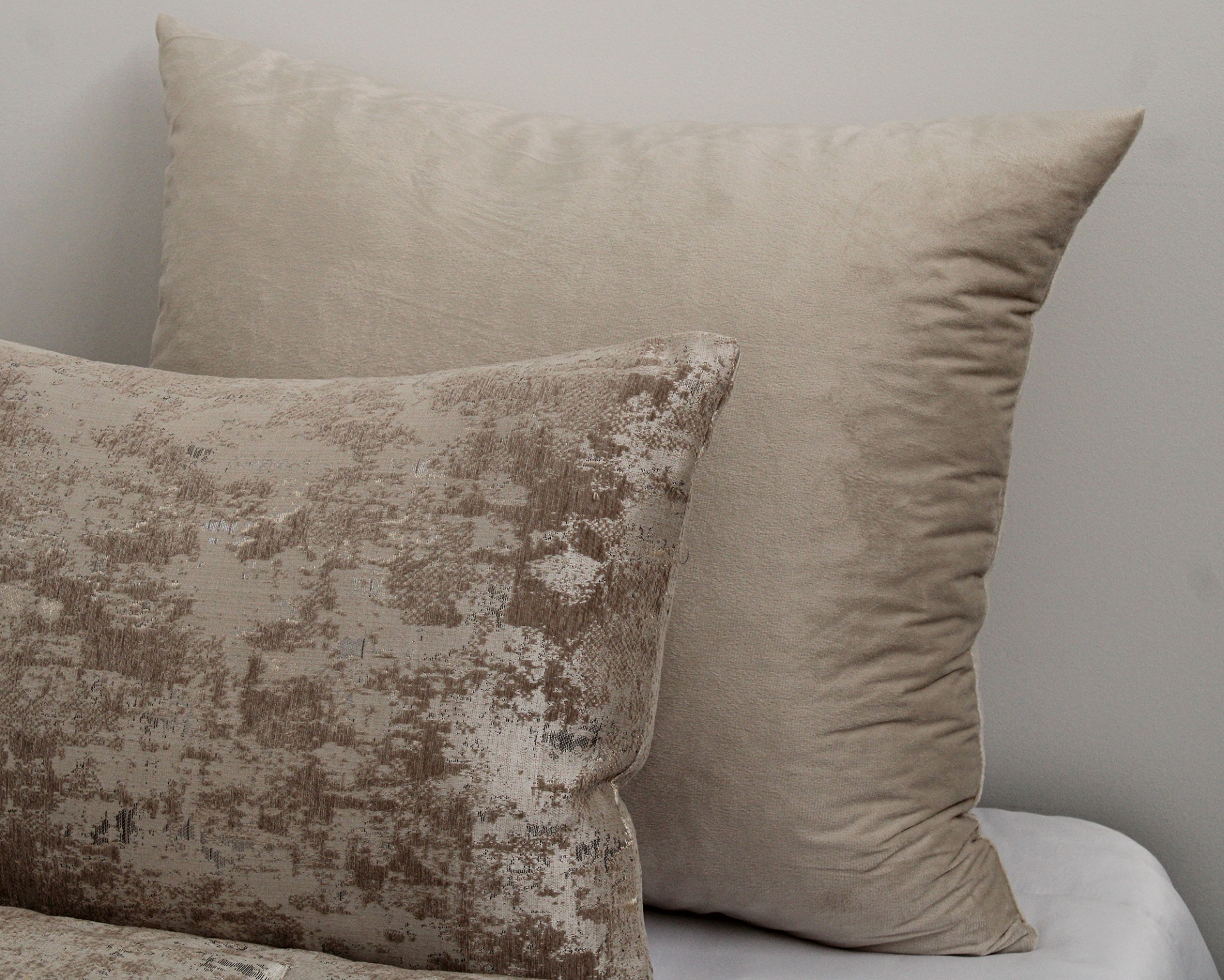 Duas almofadas decorativas bege com tecidos diferentes sobre superfície branca