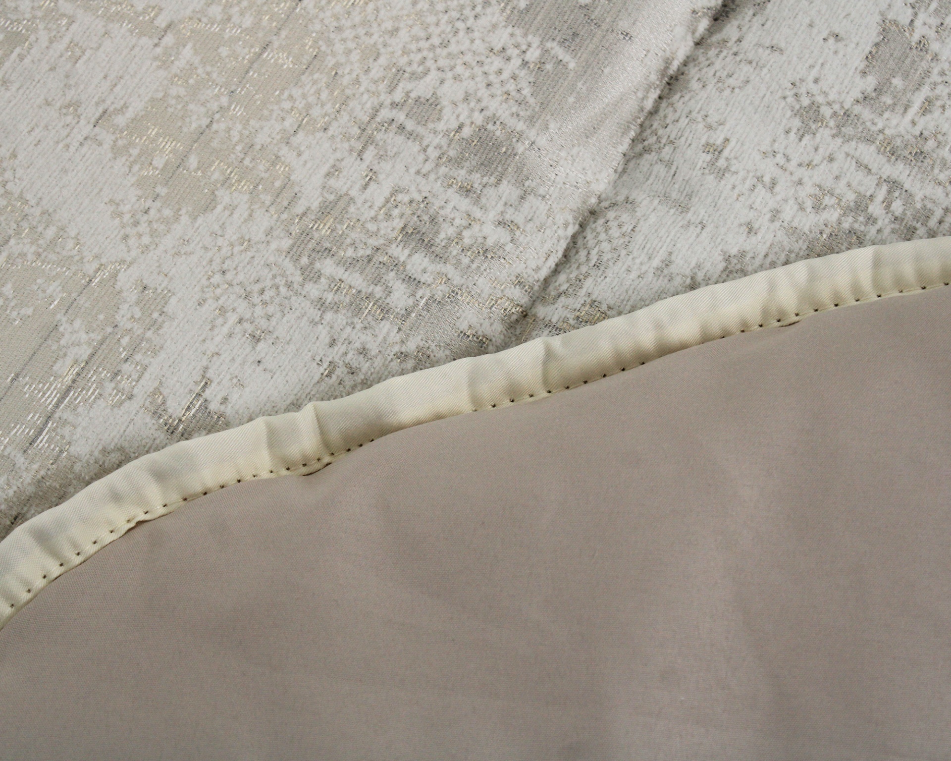 Tecido com padrão texturizado bege e dourado com borda costurada e superfície lisa castanha clara