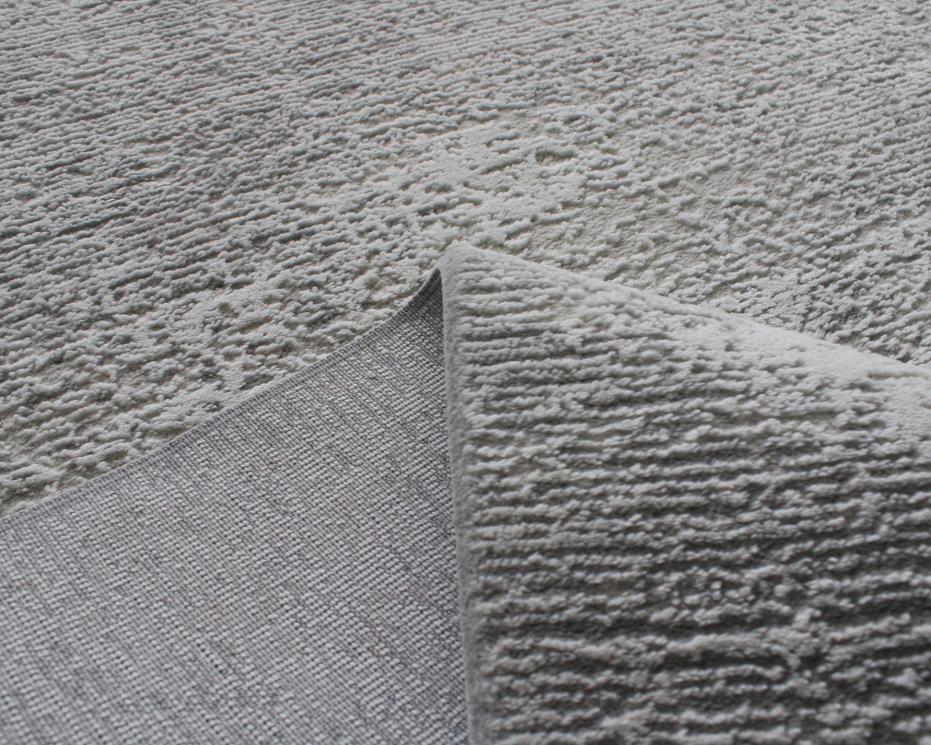 Tapete cinzento com textura elevada e padrão irregular, mostrando o verso