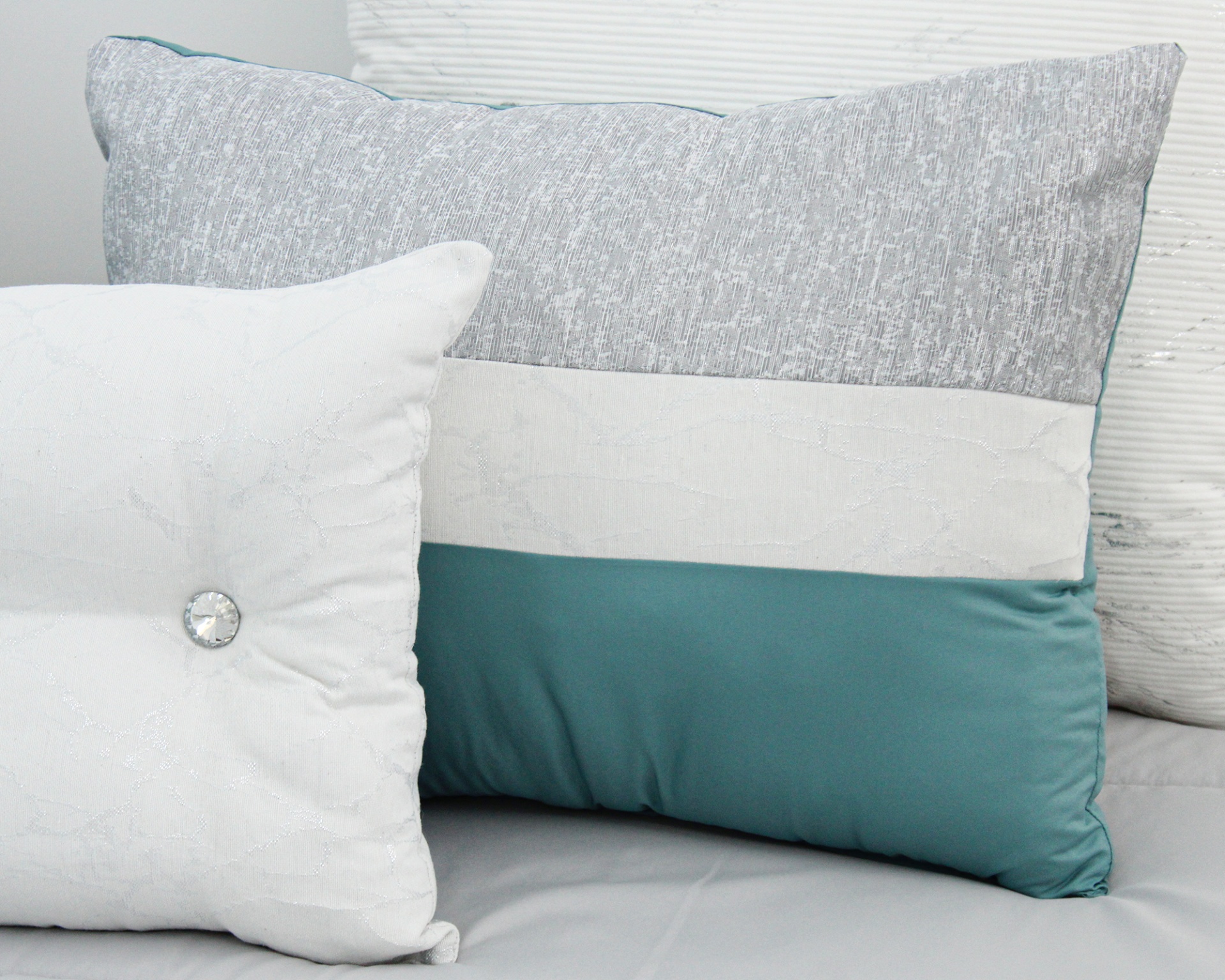 Duas almofadas decorativas, uma cinza, branca e azul-esverdeada, outra branca com botão prateado