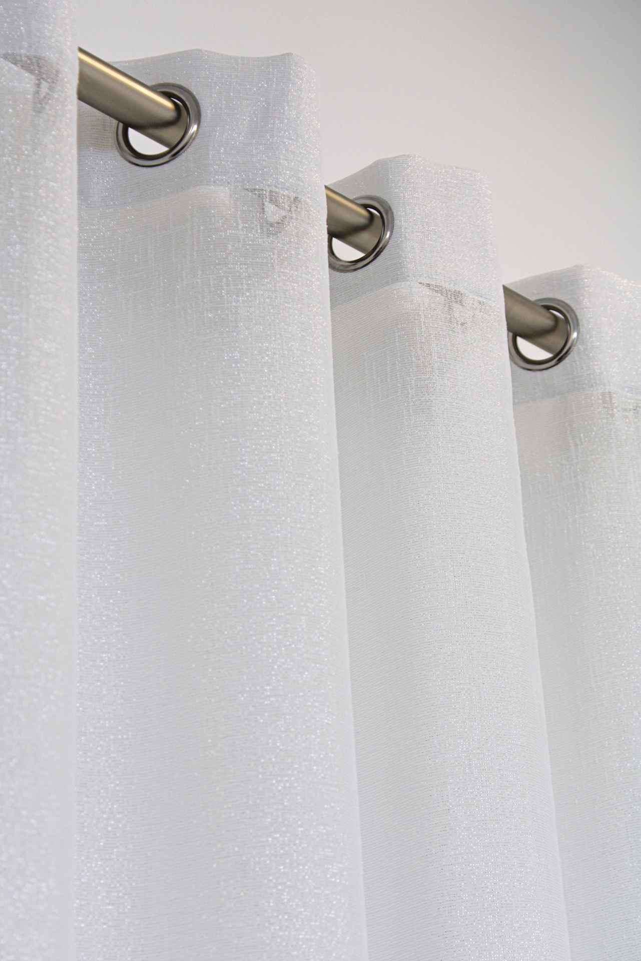 Cortina branca translúcida com ilhóses prateados pendurada numa barra metálica.