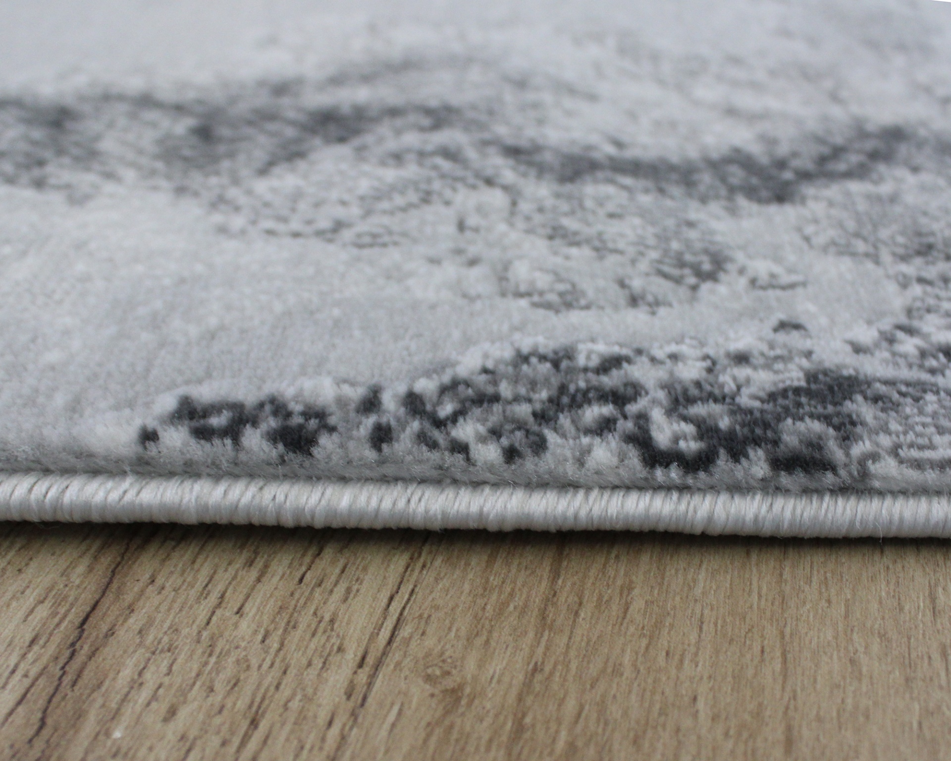 Tapete cinzento claro com borda costurada sobre chão de madeira