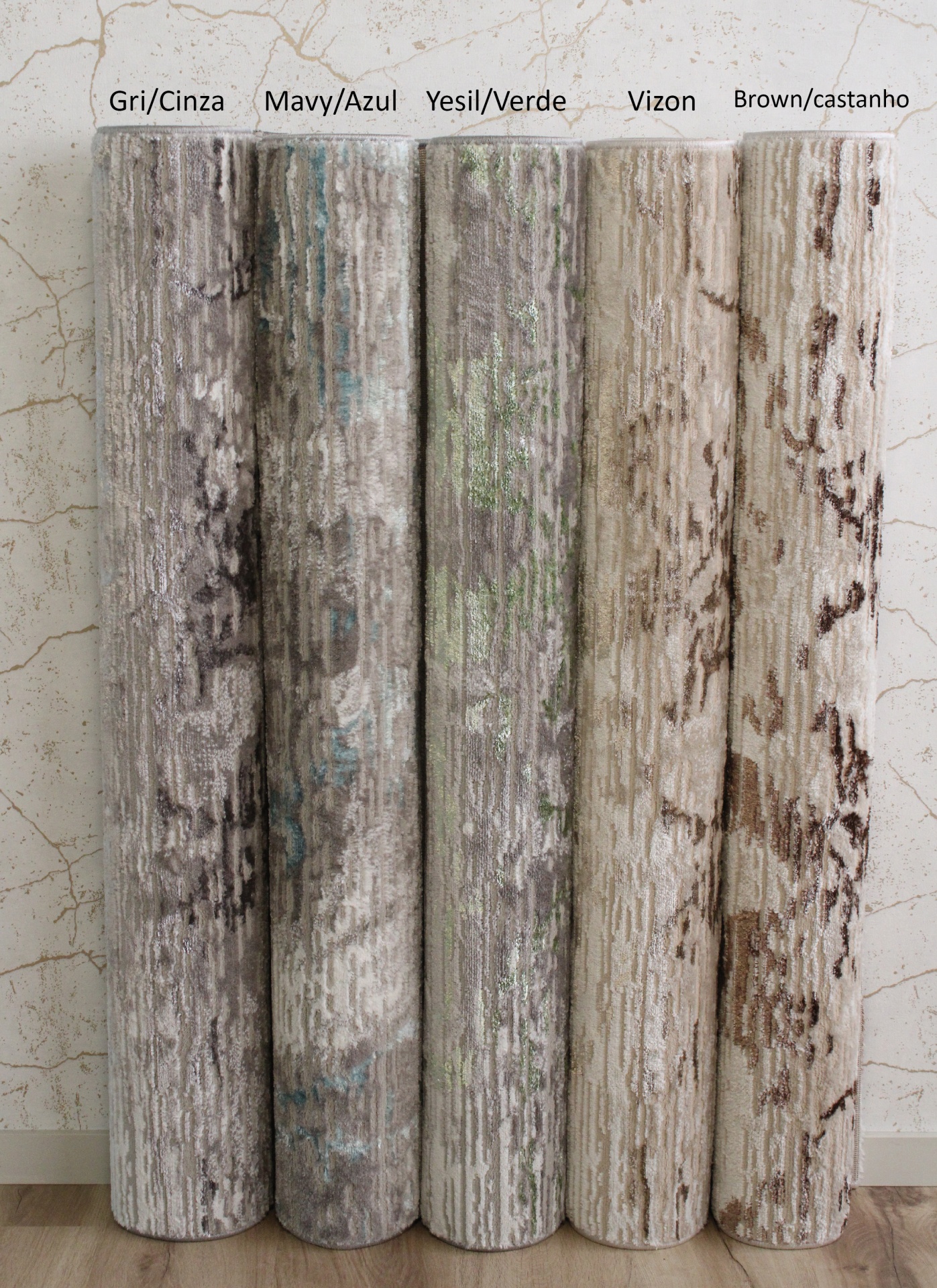 Cinco tapetes enrolados em diferentes cores e padrões contra uma parede clara