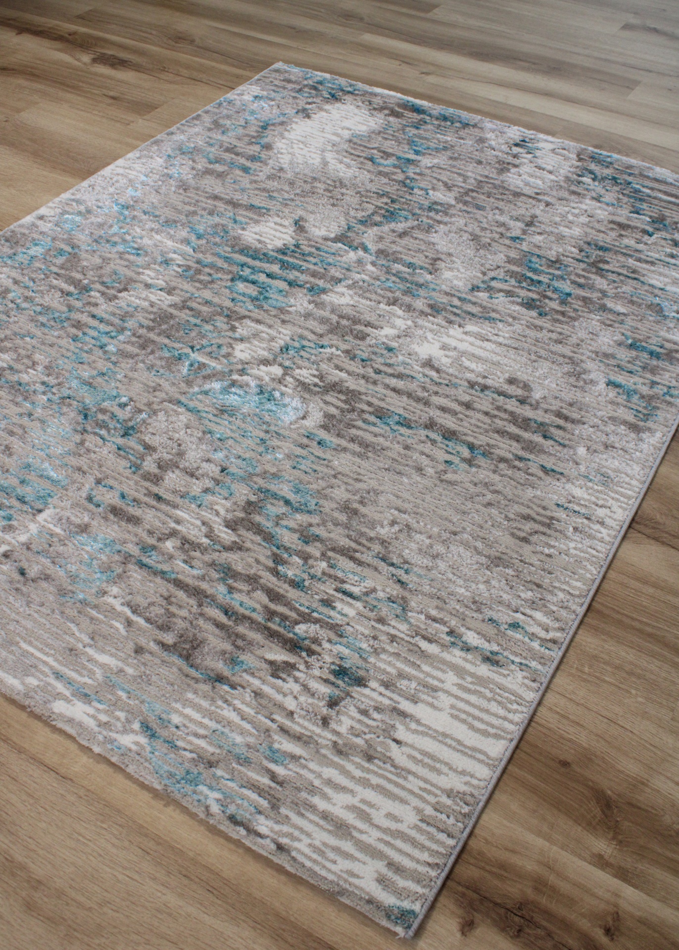 Tapete abstrato cinza, bege e azul-petróleo sobre chão de madeira