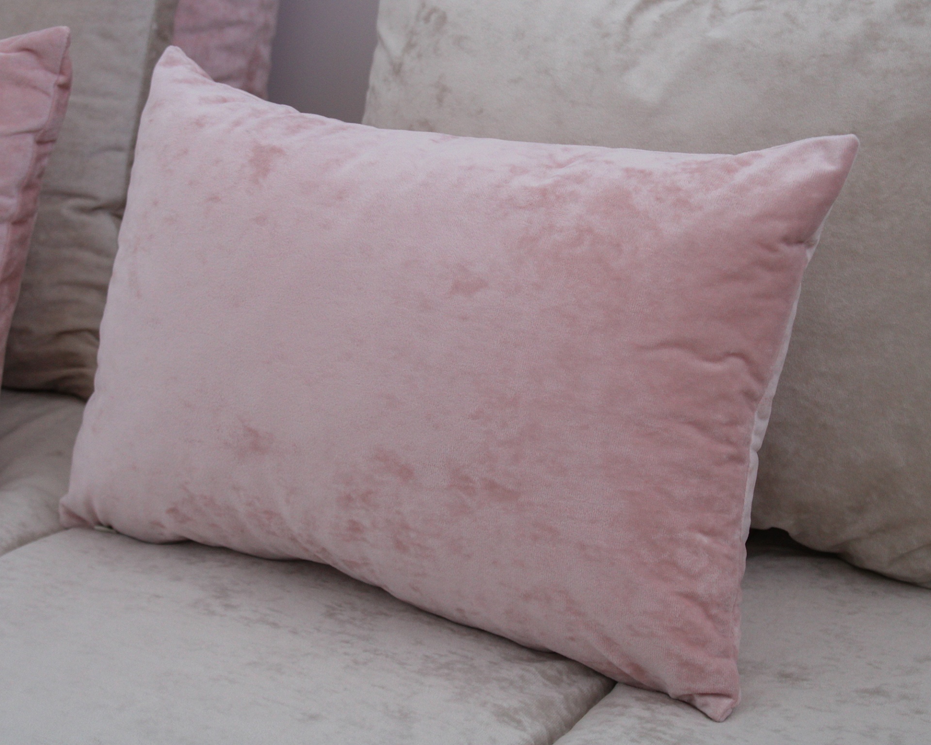 Almofada cor de rosa aveludada sobre sofá cinzento claro