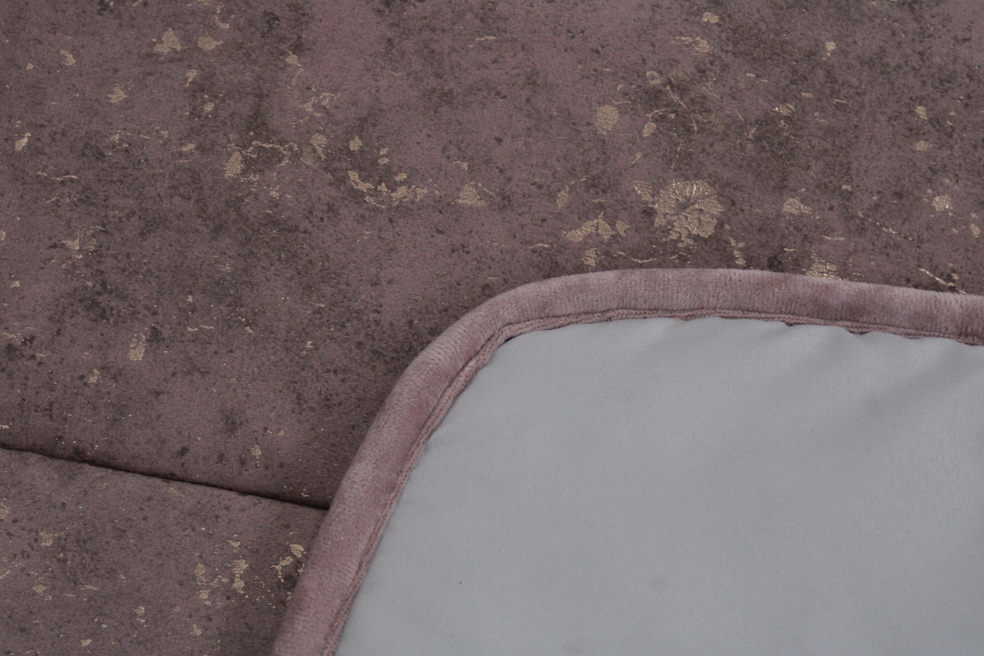 Tecido violeta com padrão dourado e canto de tapete cinzento com borda violeta