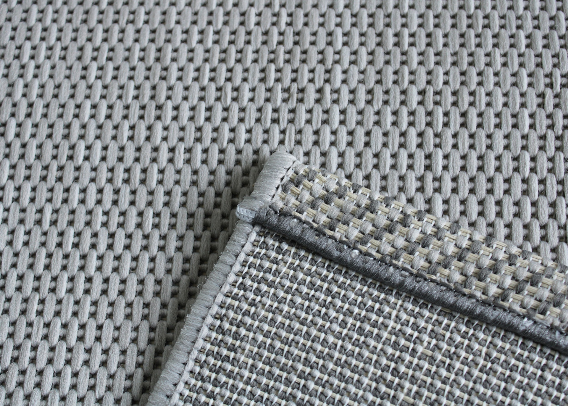 Tapete cinza trançado com borda cinza e dobra mostrando o verso