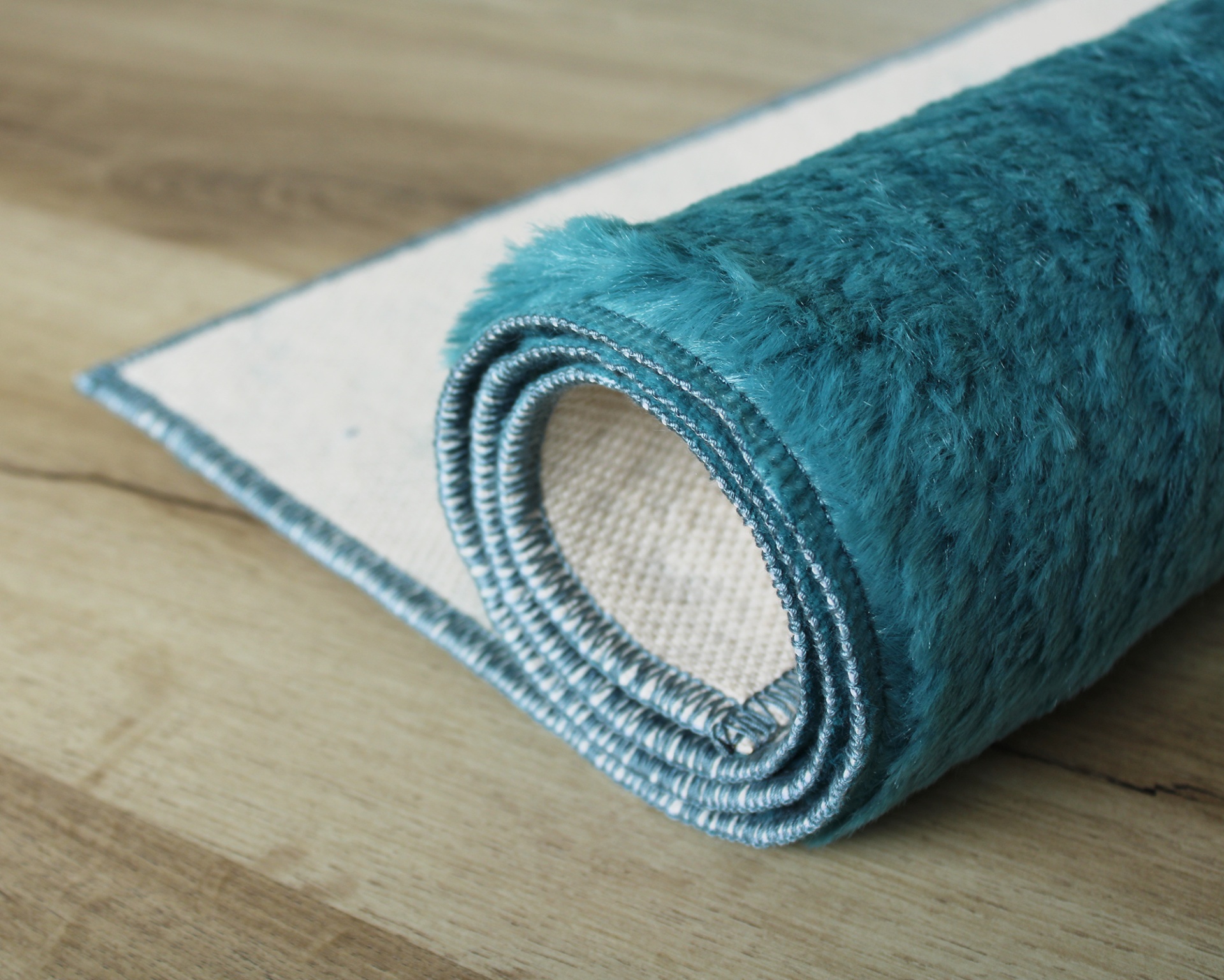 Tapete azul turquesa felpudo enrolado sobre chão de madeira