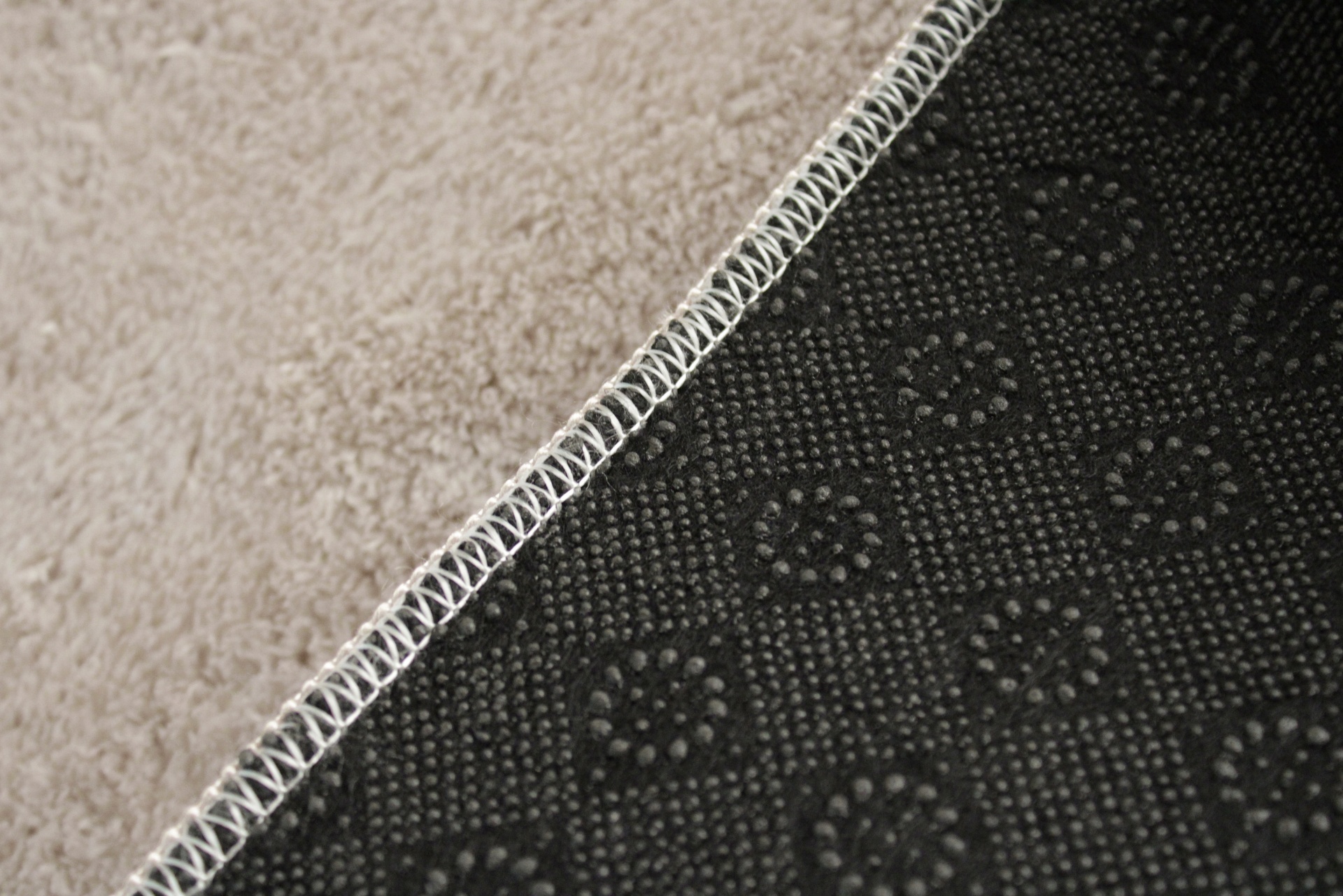 Detalhe da parte de trás de um tapete preto com padrão e costura branca, sobre chão bege
