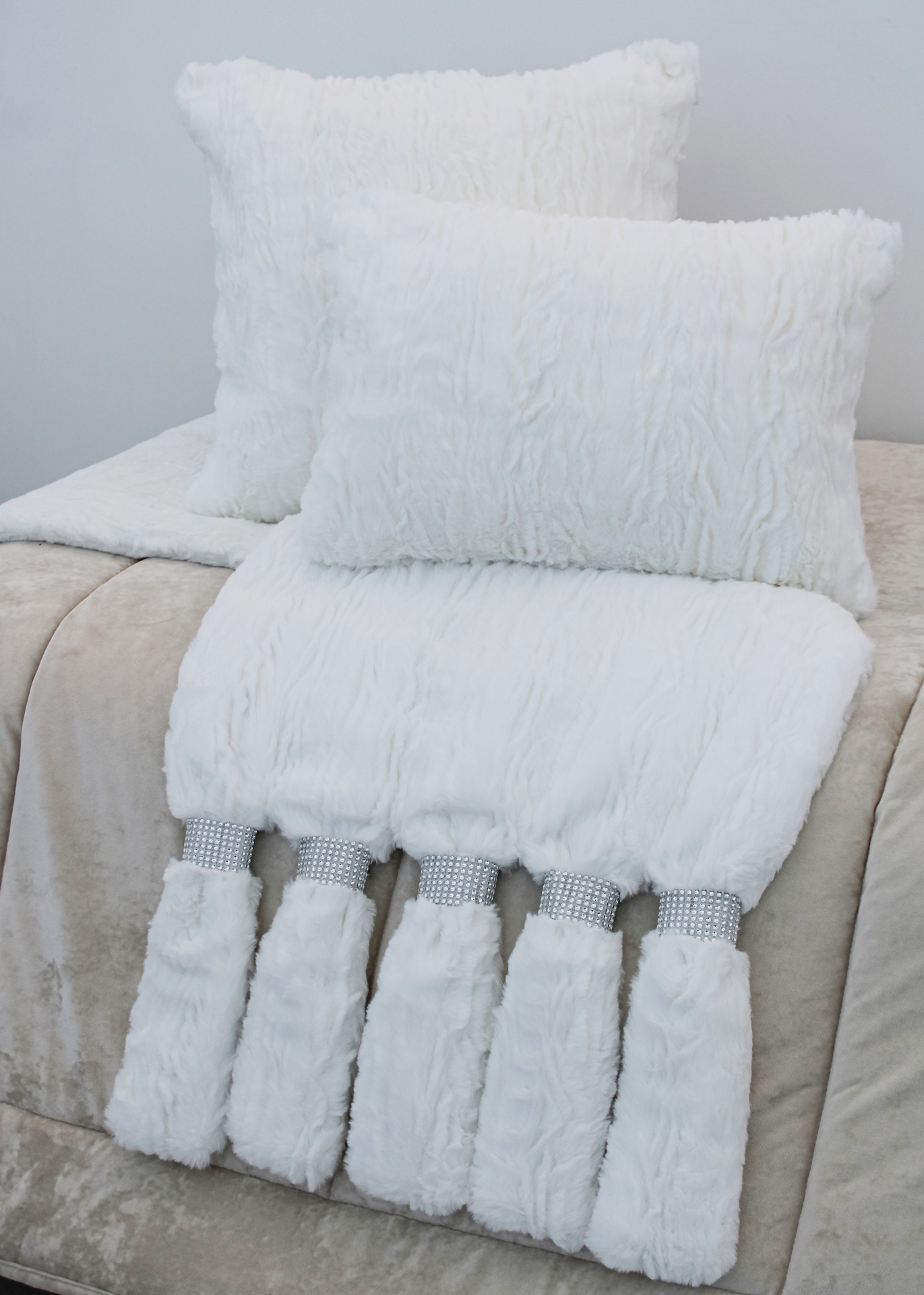 Almofadas e manta branca felpuda com franjas e detalhes prateados sobre sofá cinza