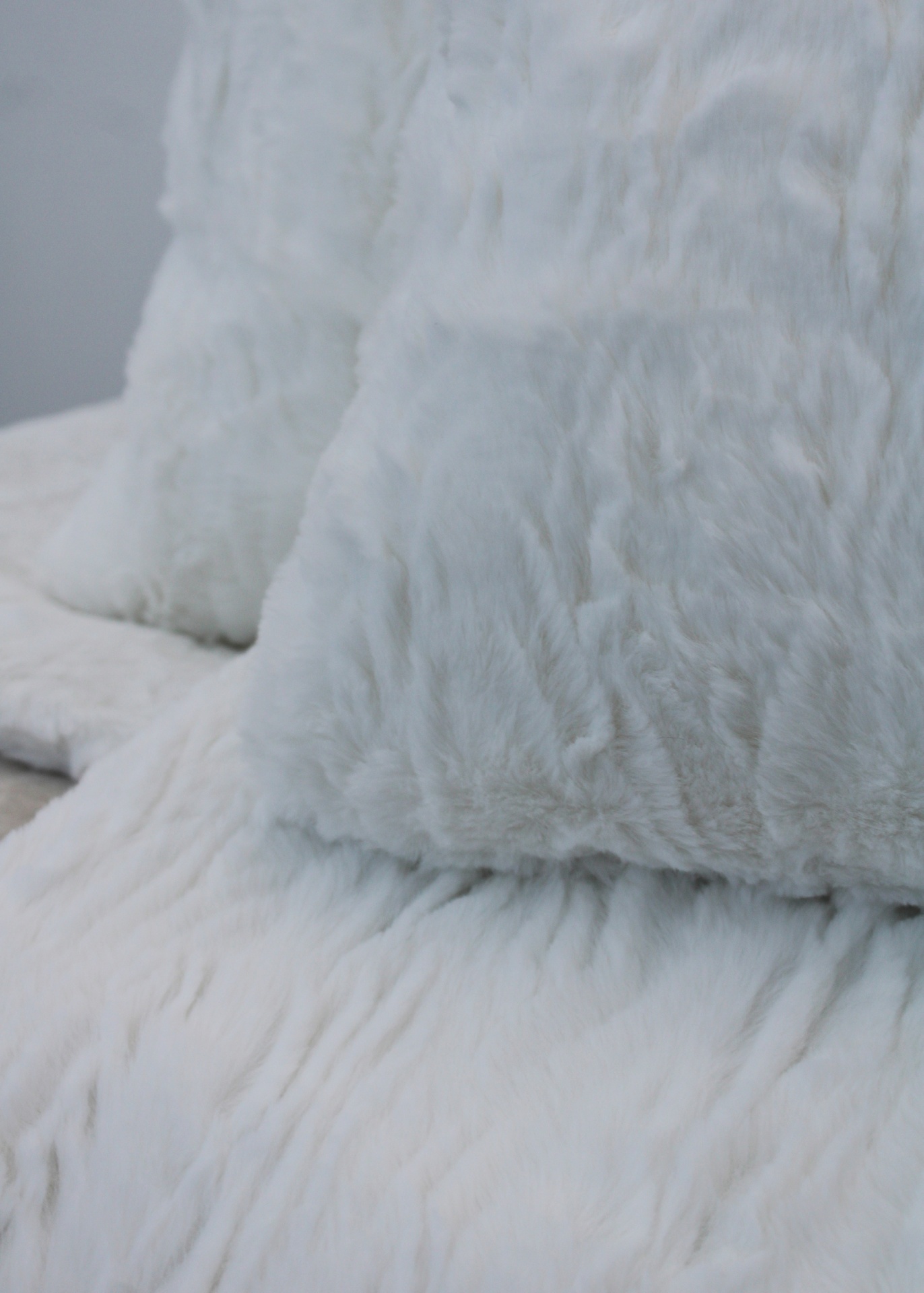 Travesseiro e manta felpudos brancos sobre superfície clara