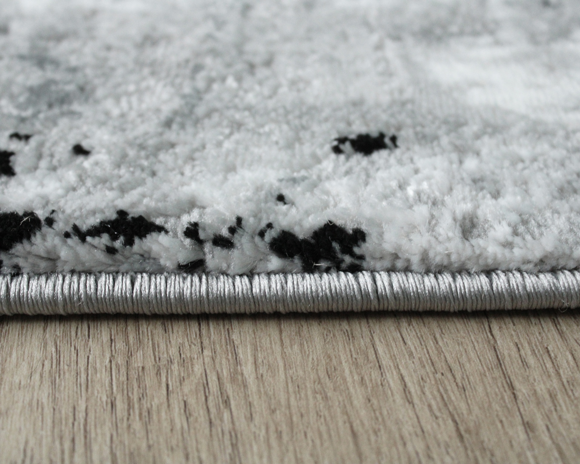 Tapete branco com manchas pretas e acabamento lateral em costura branca sobre piso de madeira