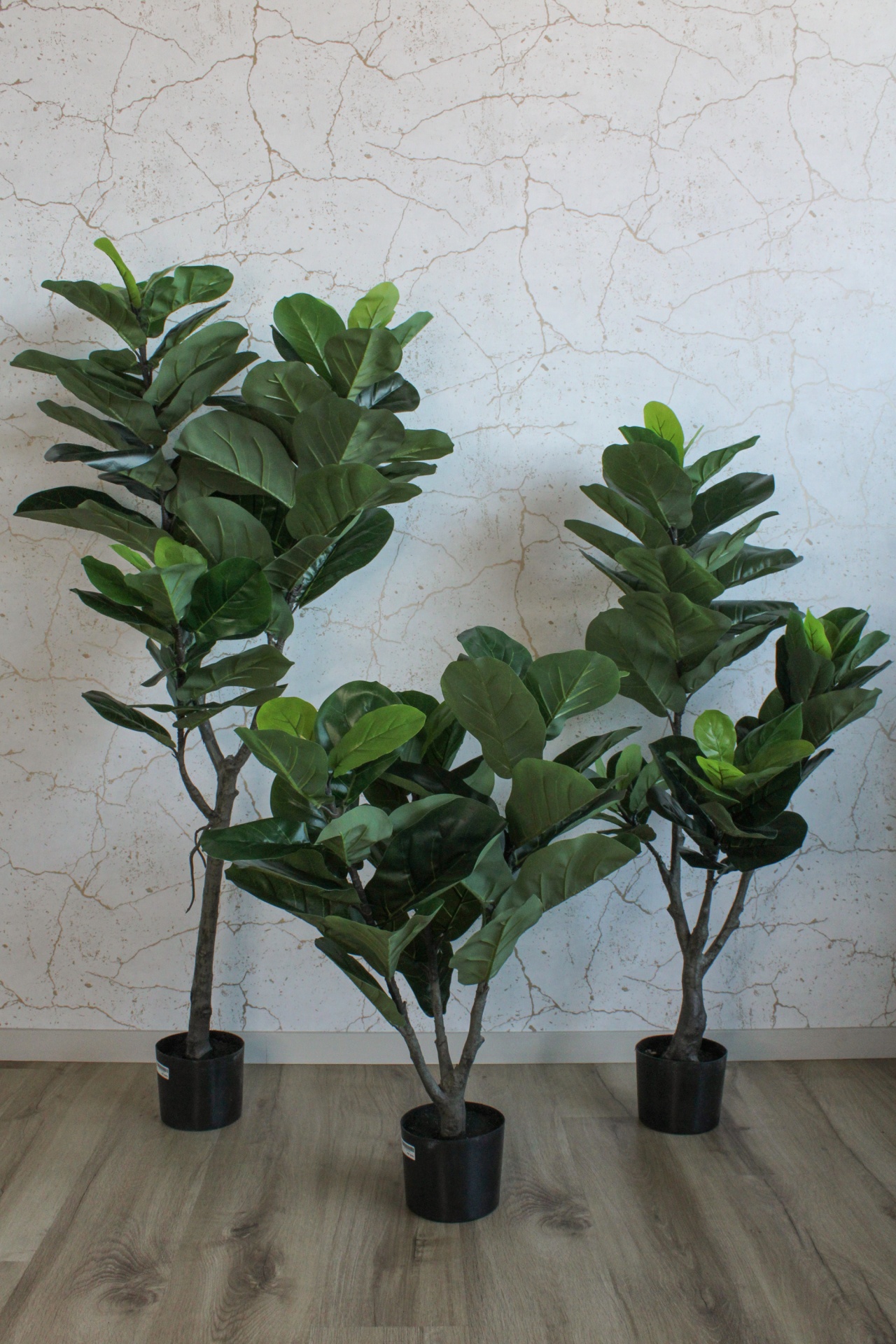 Três plantas artificiais em vasos pretos com folhas verdes largas e textura lisa