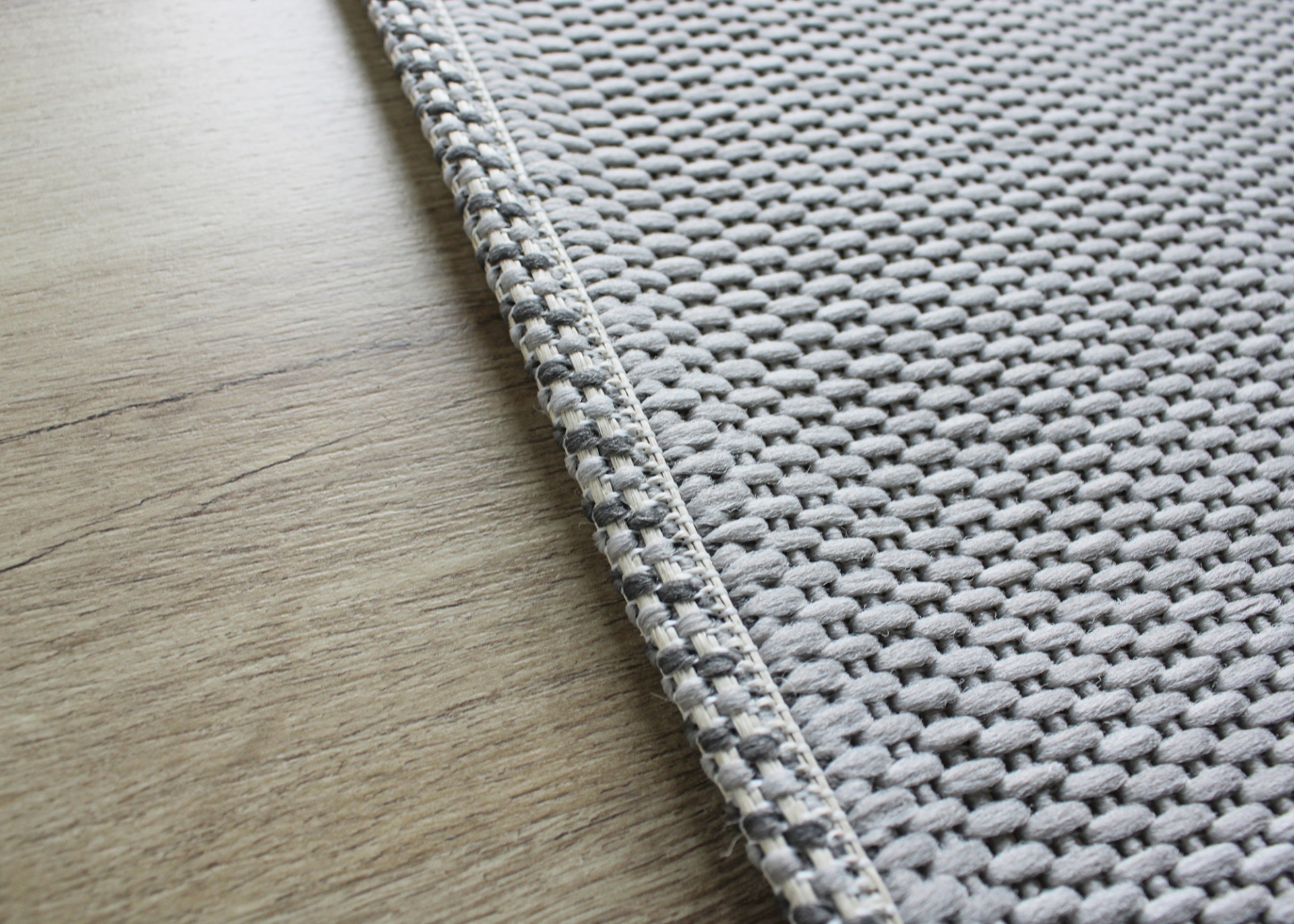 Tapete cinza com textura em relevo sobre piso de madeira clara.