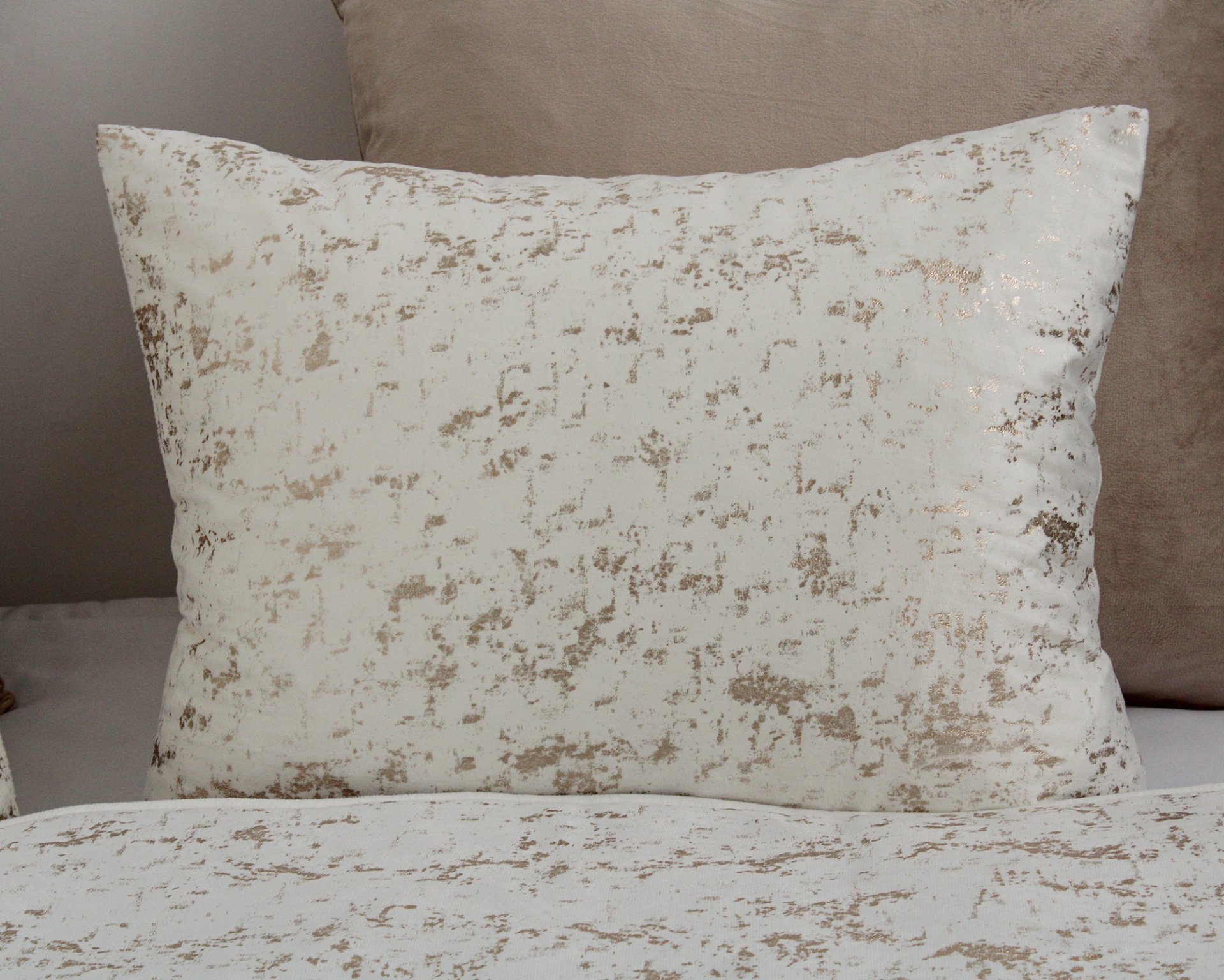 Almofada branca com padrão bege e dourado sobre cama