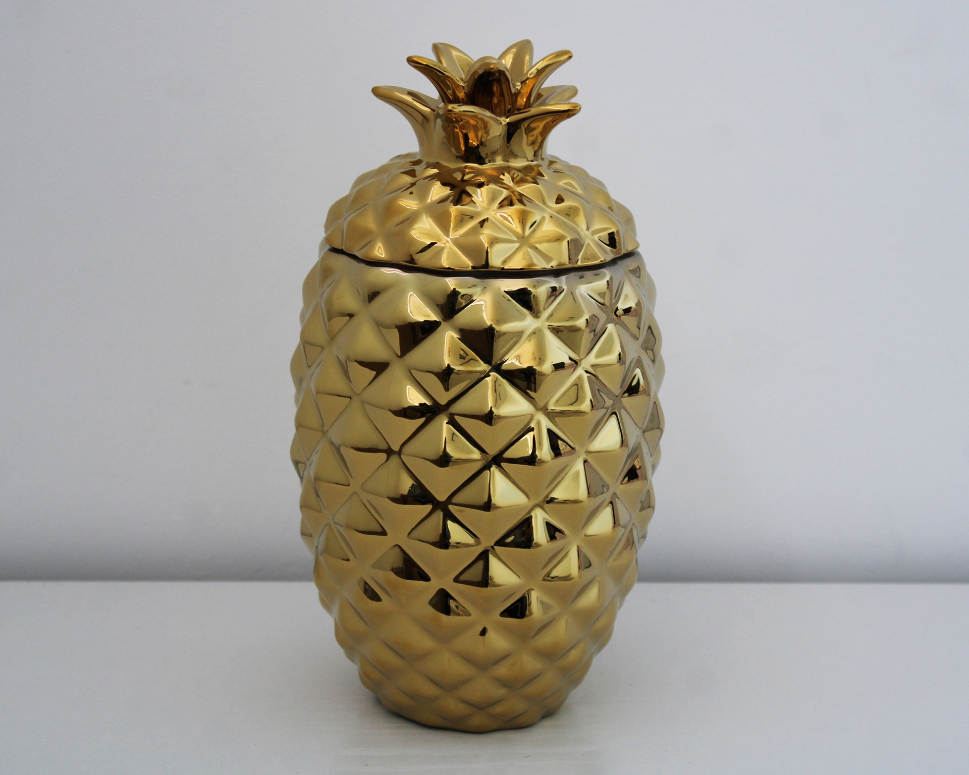 Recipiente dourado em forma de ananás com tampa decorativa.