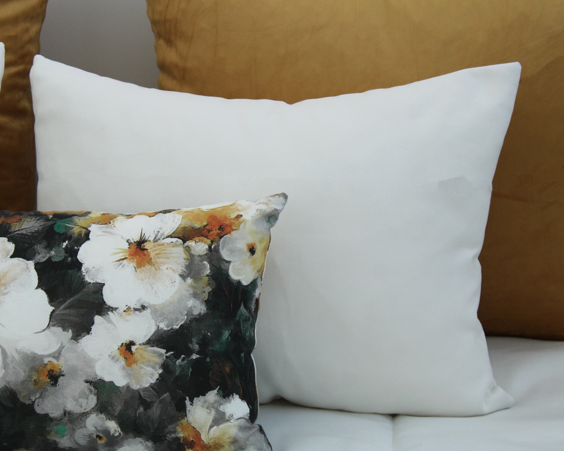 Três almofadas sobre cama, uma branca, uma marrom e uma com padrão floral colorido.