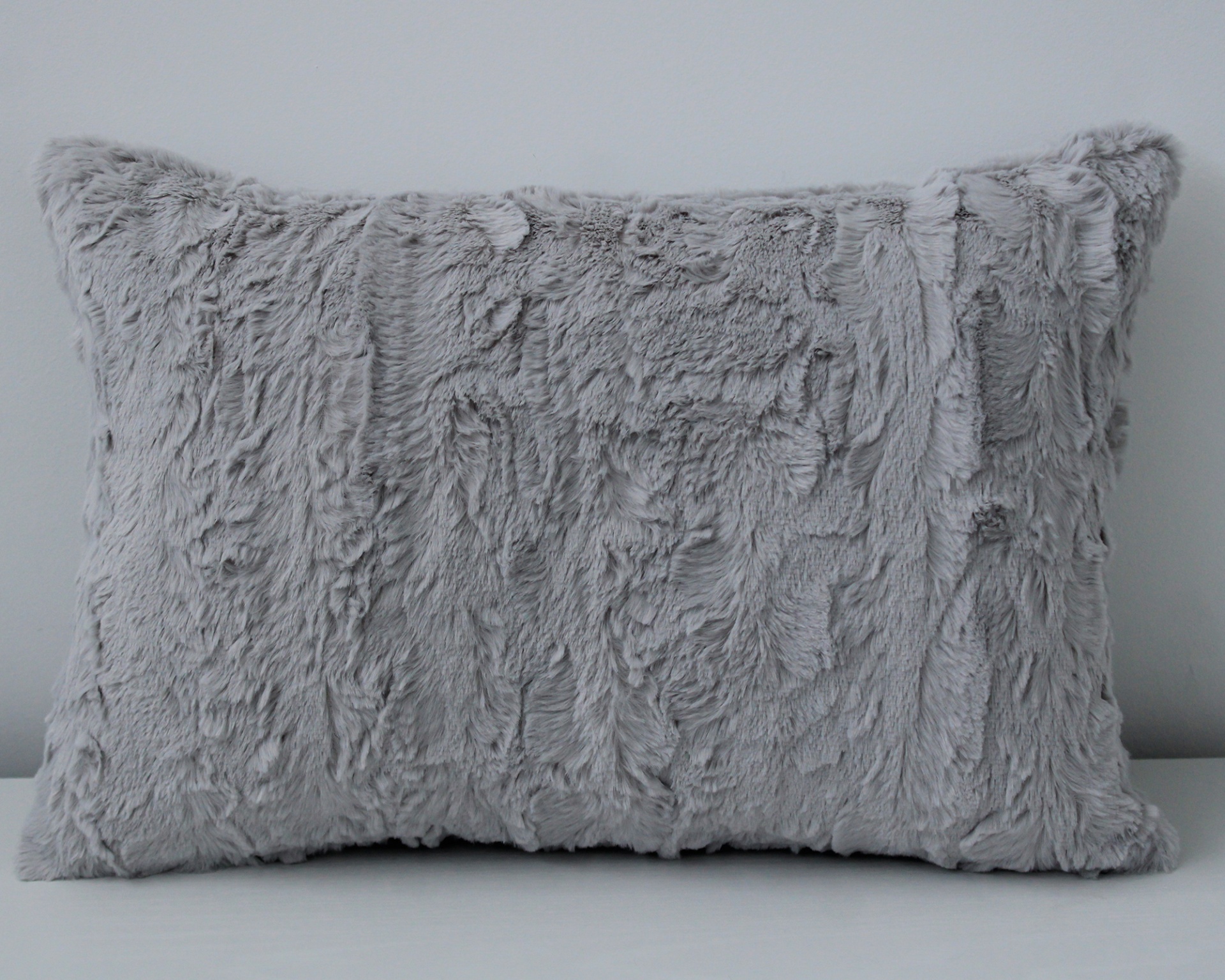 Almofada cinza peluda retangular sobre superfície branca