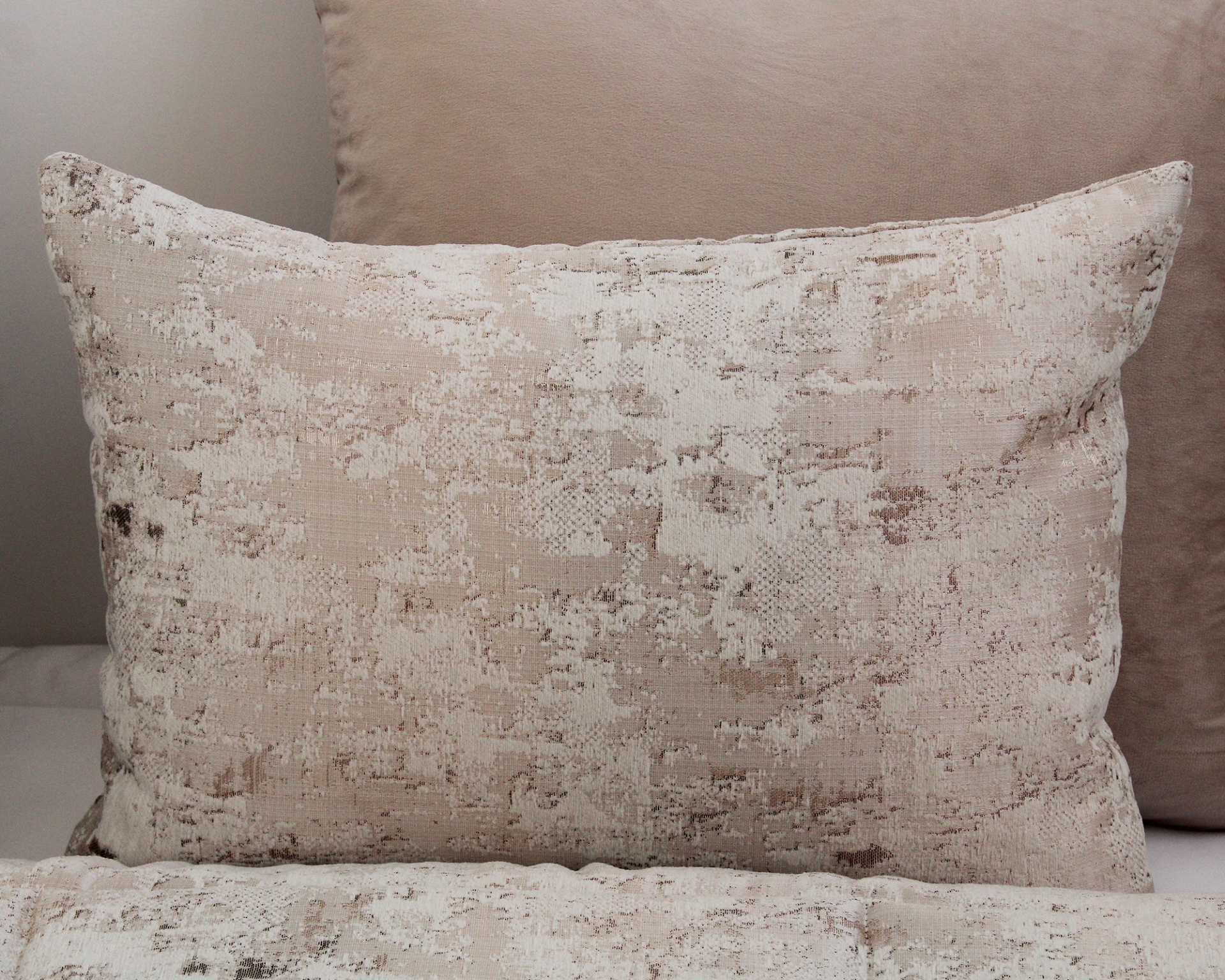 Travesseiro decorativo bege com padrão abstrato colocado sobre almofada bege