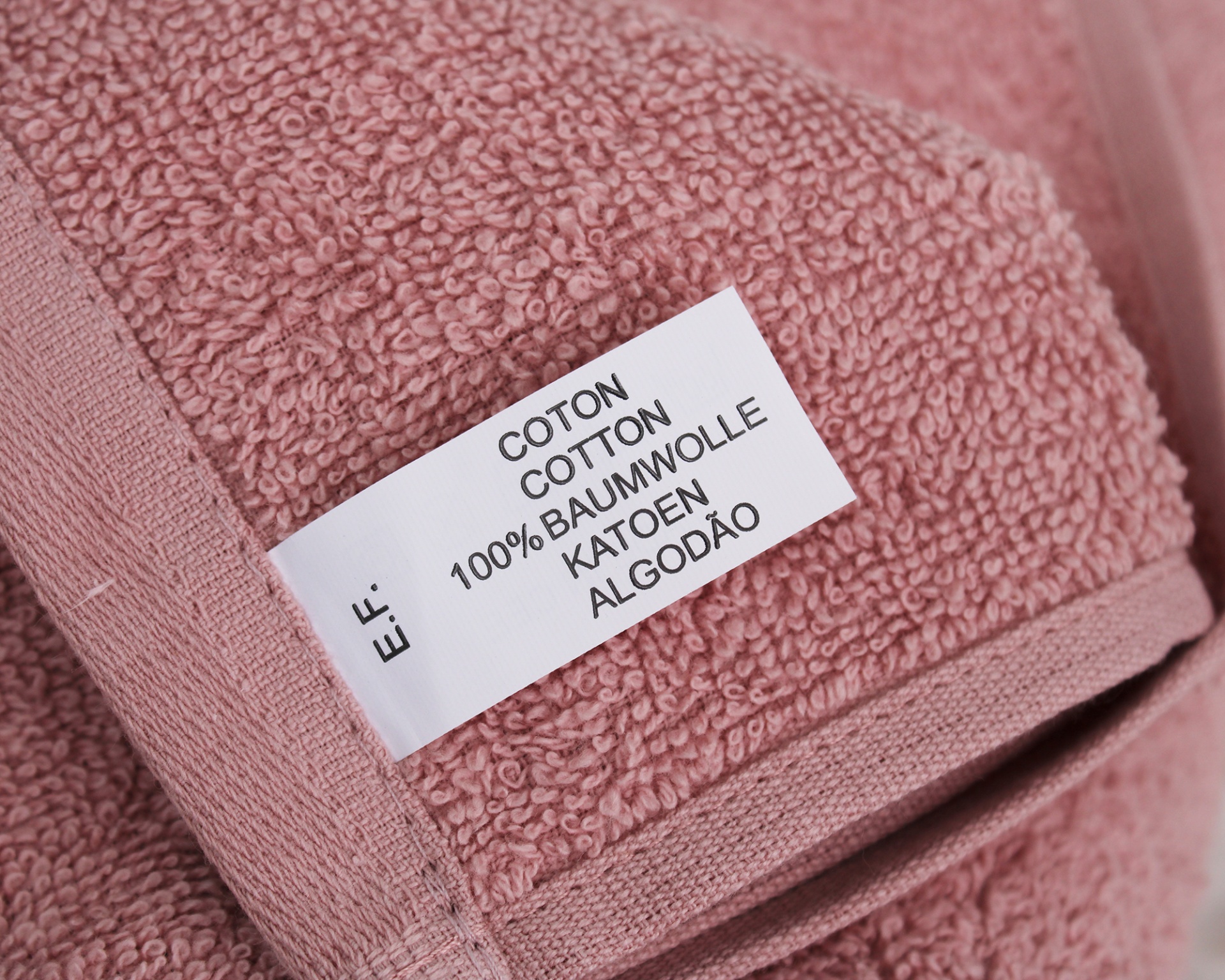 Toalha rosa de algodão com etiqueta indicando 100% algodão