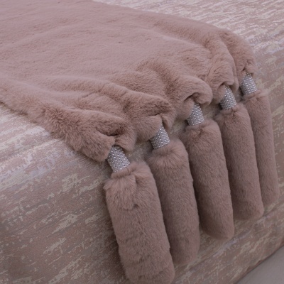 Manta felpuda rosa clara com tasséis decorativos sobre tecido com padrão rosa e bege