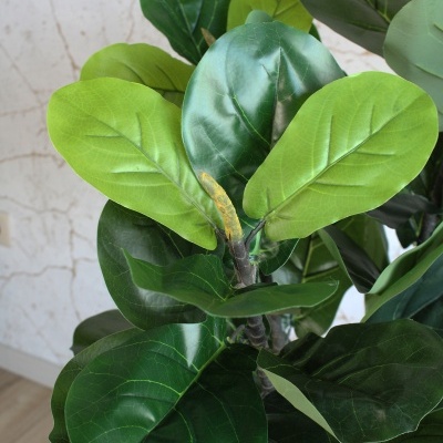 Planta artificial com folhas verdes em vaso preto com borda dourada junto a parede bege