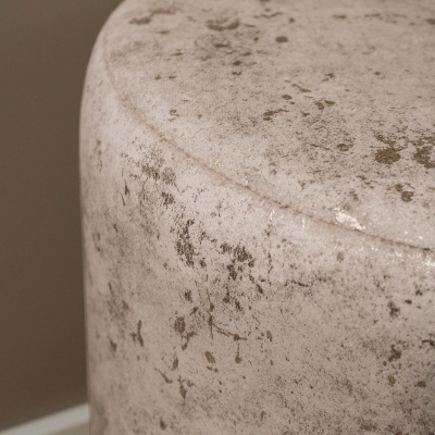 Pufe cilíndrico em tecido aveludado bege com manchas castanhas, em ambiente interior