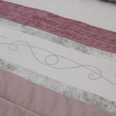 Detalhe de têxtil de cama rosa, branco e cinza com padrões e texturas variadas