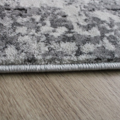 Detalhe da borda de tapete cinza com padrão abstrato sobre chão de madeira clara