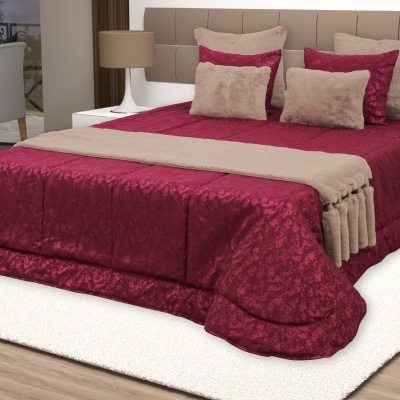 Cama de casal com colcha floral vermelho vinho, manta bege peluda e almofadas, quarto com carpete branco e piso madeira clara