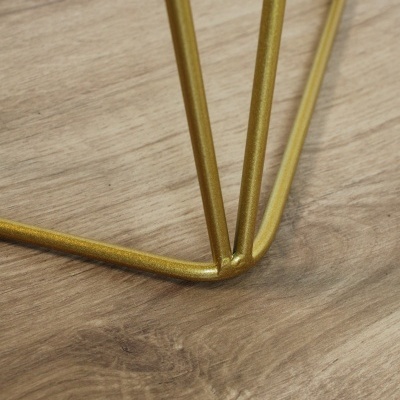 Base triangular dourada em metal sobre chão de madeira clara