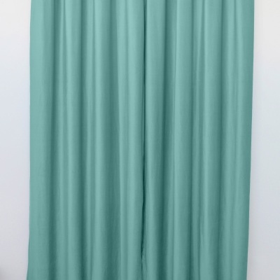 Cortina azul turquesa em tecido com ilhós prateados suspensa numa barra metálica contra parede branca