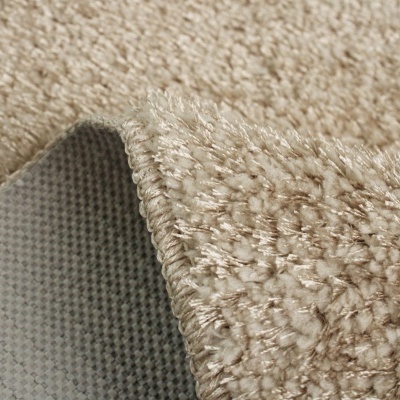 Tapete bege com textura densa e verso antiderrapante cinzento sobre tapete de pelo curto bege