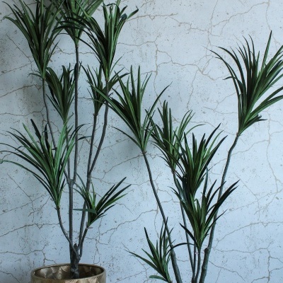 Duas plantas artificiais em vasos dourados com padrão circular, parede branca rachada ao fundo